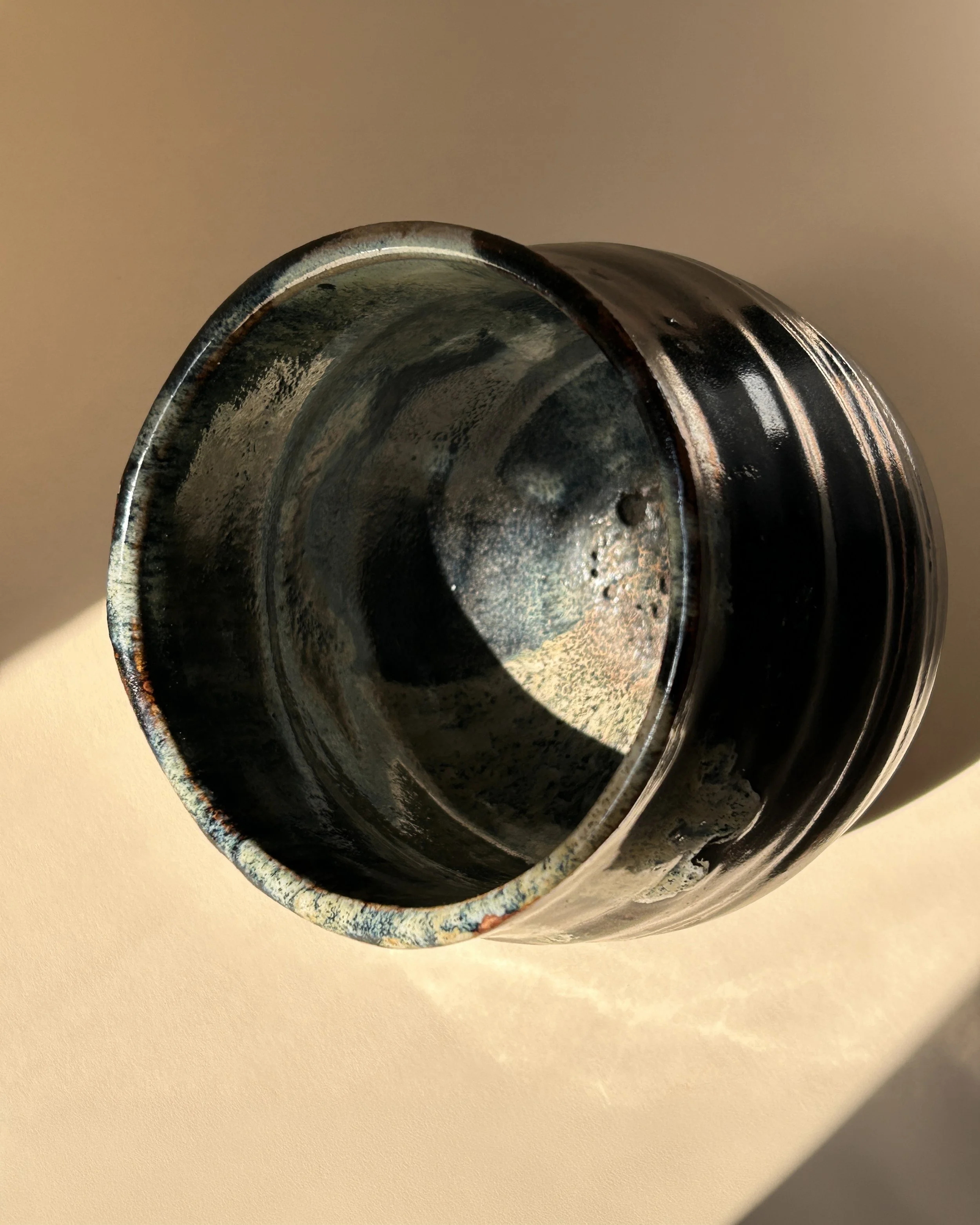 Signed handmade studio pottery vessel with glossy black glaze, rust-colored bands and cascading cream and blue green glaze decoration.