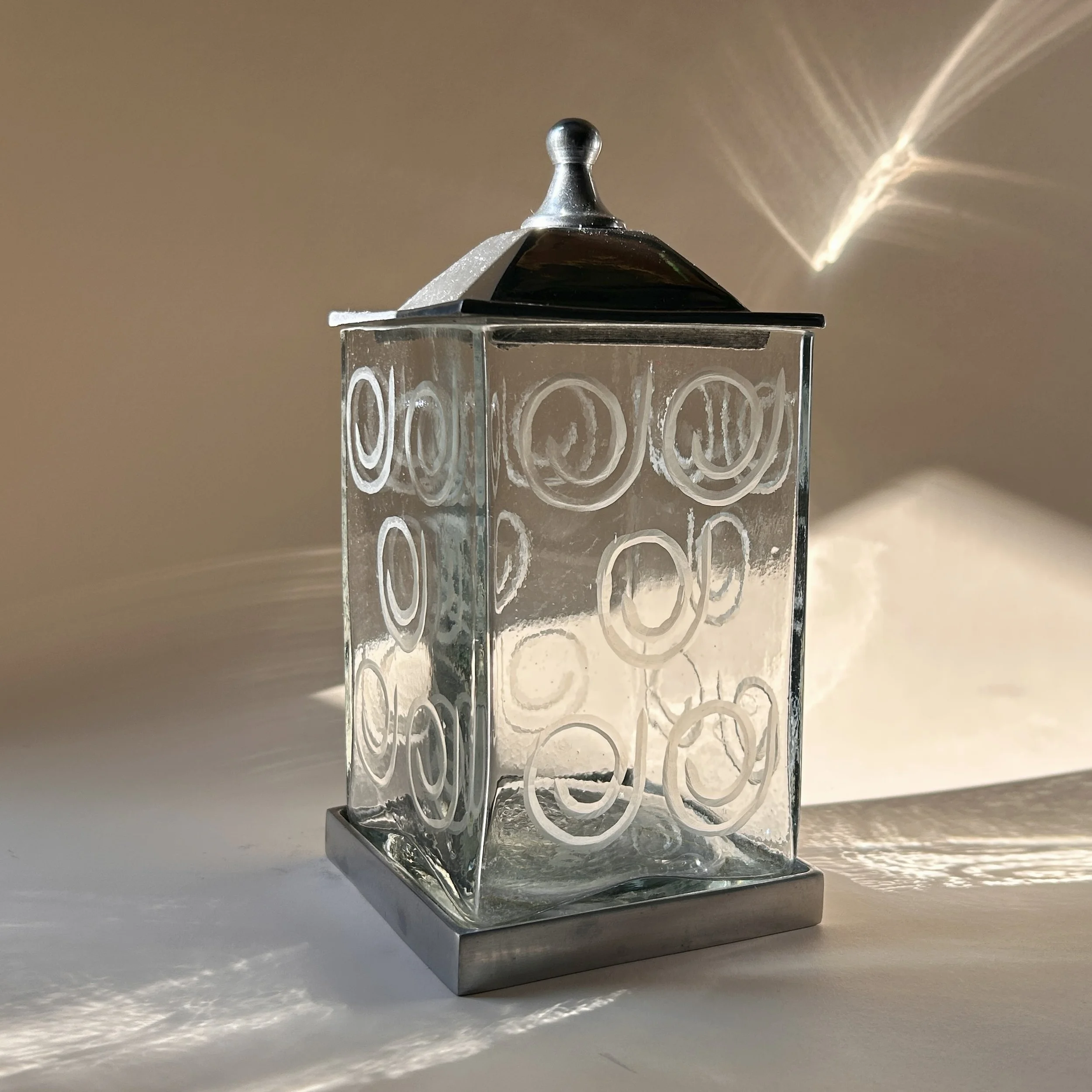 Contemporary square clear glass canisters with etched spiral patterns, silver-tone metal bases, and peaked metal lids in two different heights.
