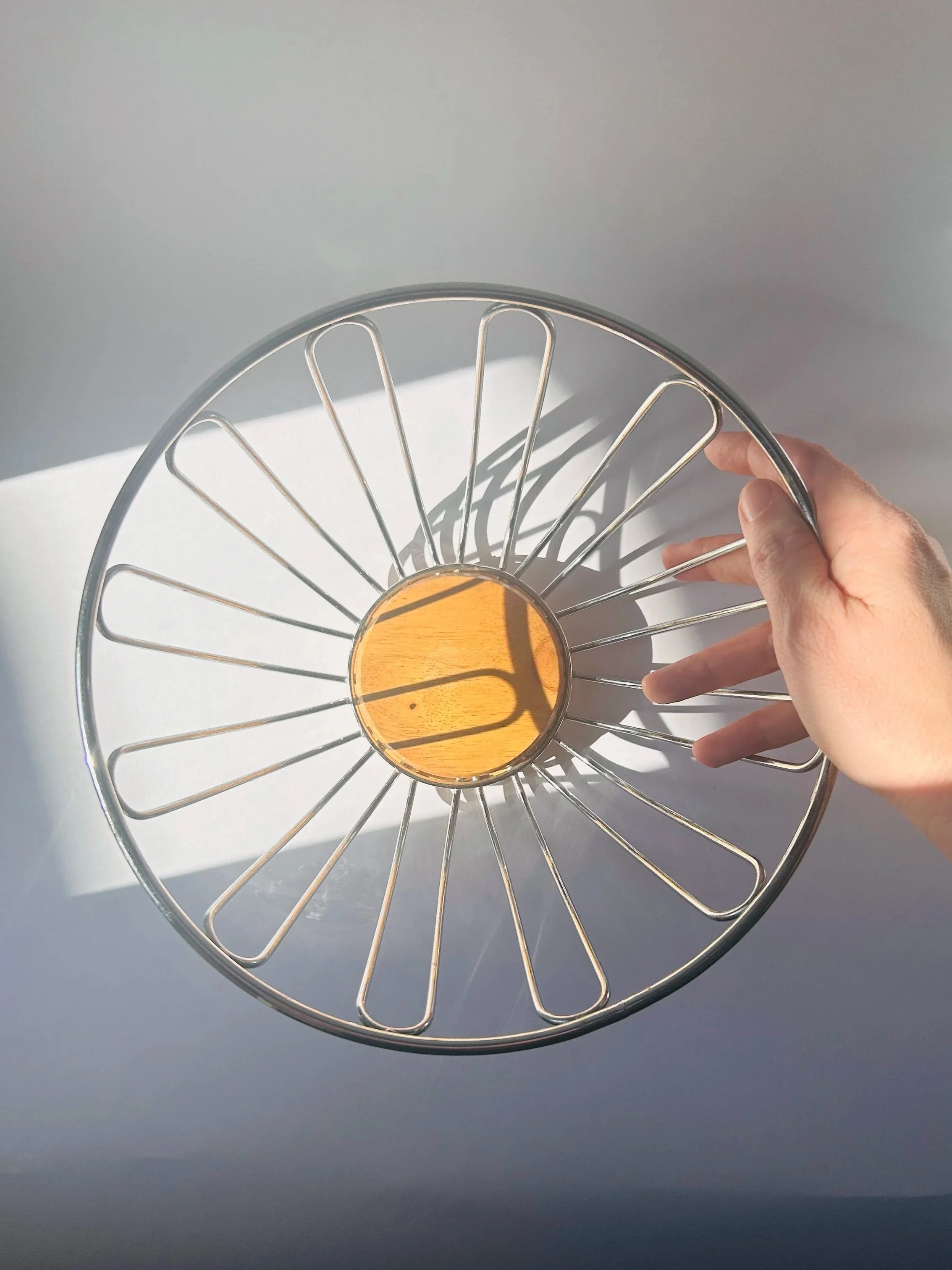 Modern stainless steel wire fruit basket with wooden base, minimalist kitchen storage bowl in natural light