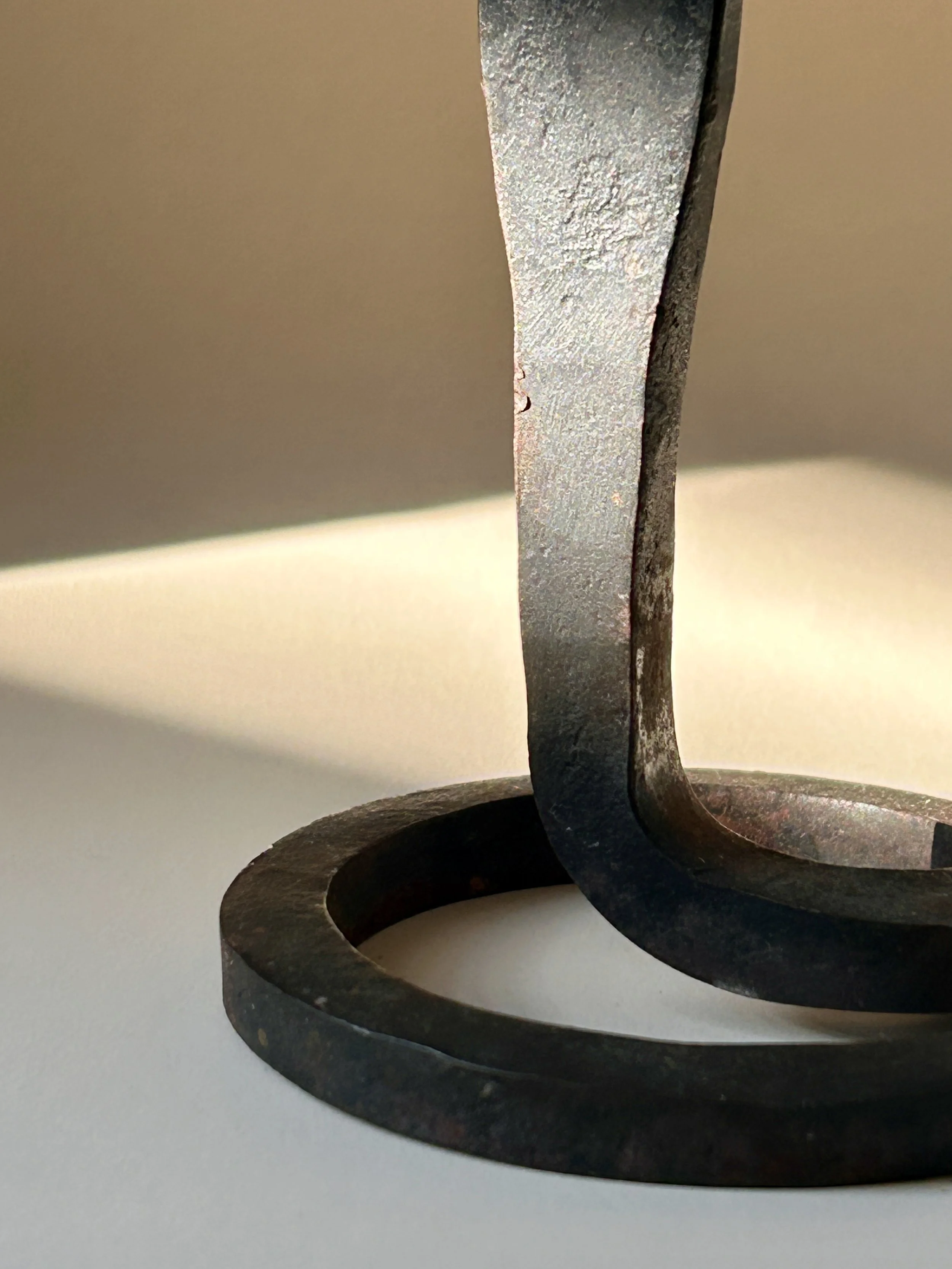 Sculptural hand forged black iron taper candlestick with a curled spiral base, slender twisted stem, and flared candle cup.
