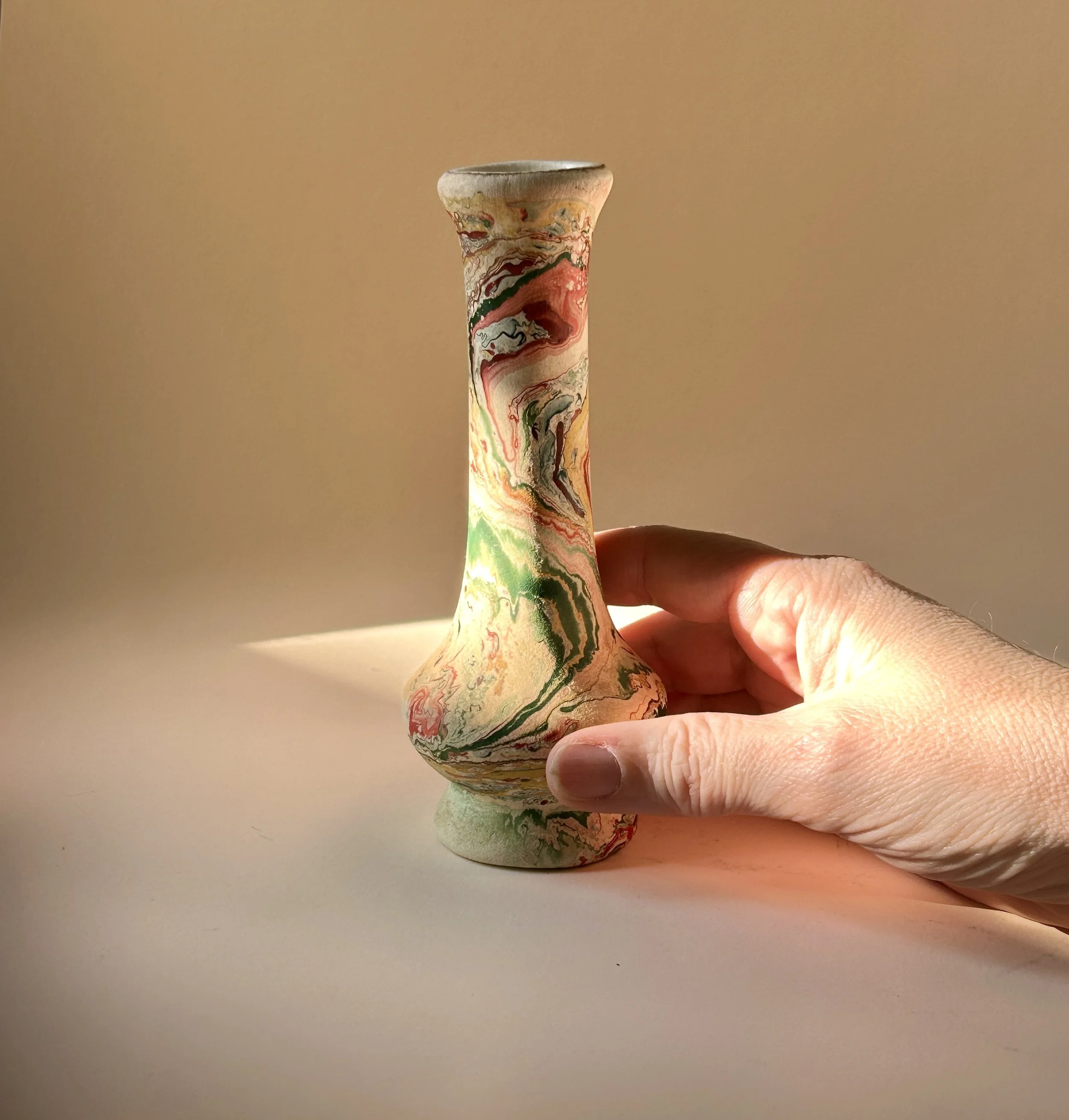 Slender vintage pottery bud vase with cream surface and swirling marbled patterns in green, coral, red, ochre, gray and black.