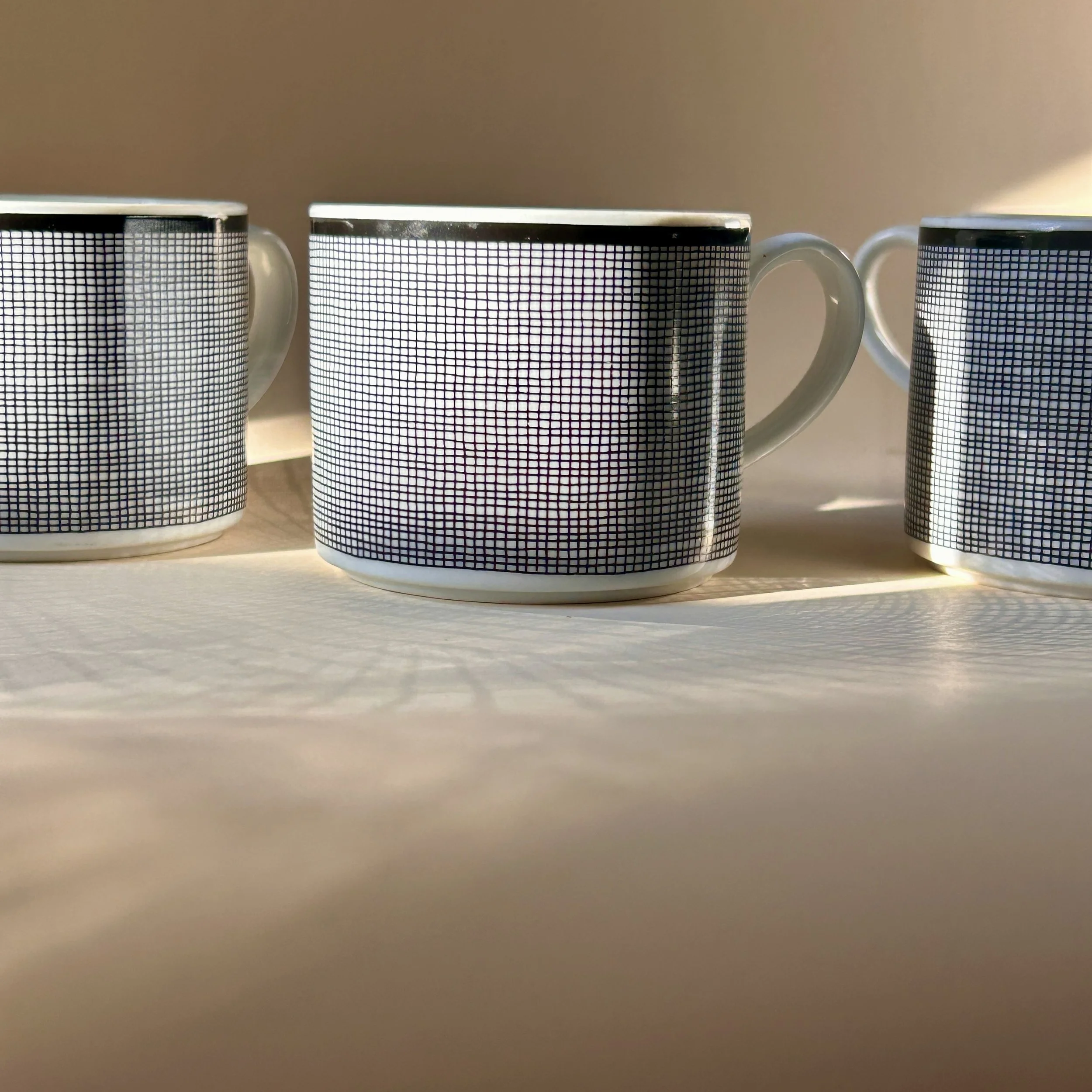 Set of four white Nancy Calhoun Chambray porcelain mugs with fine black grid pattern, black rim and white handles.