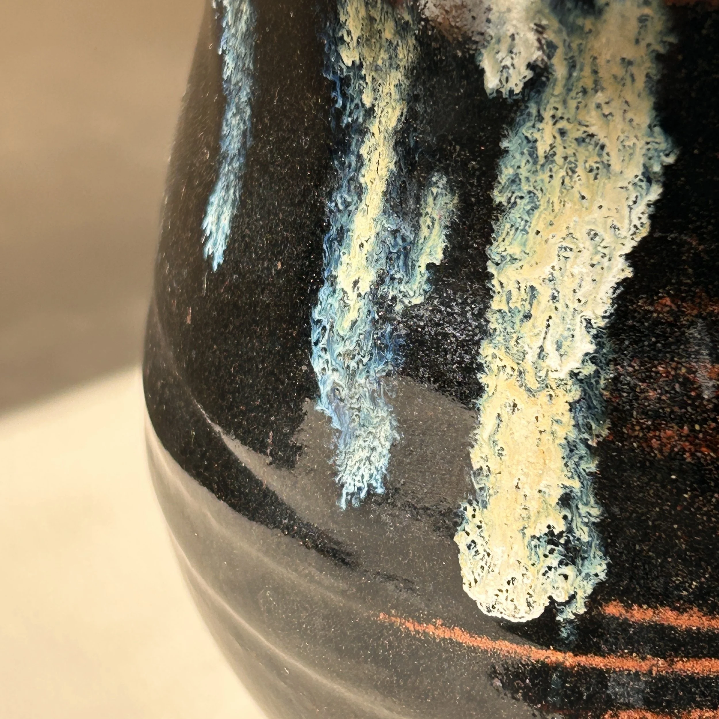 Signed handmade studio pottery vessel with glossy black glaze, rust-colored bands and cascading cream and blue green glaze decoration.