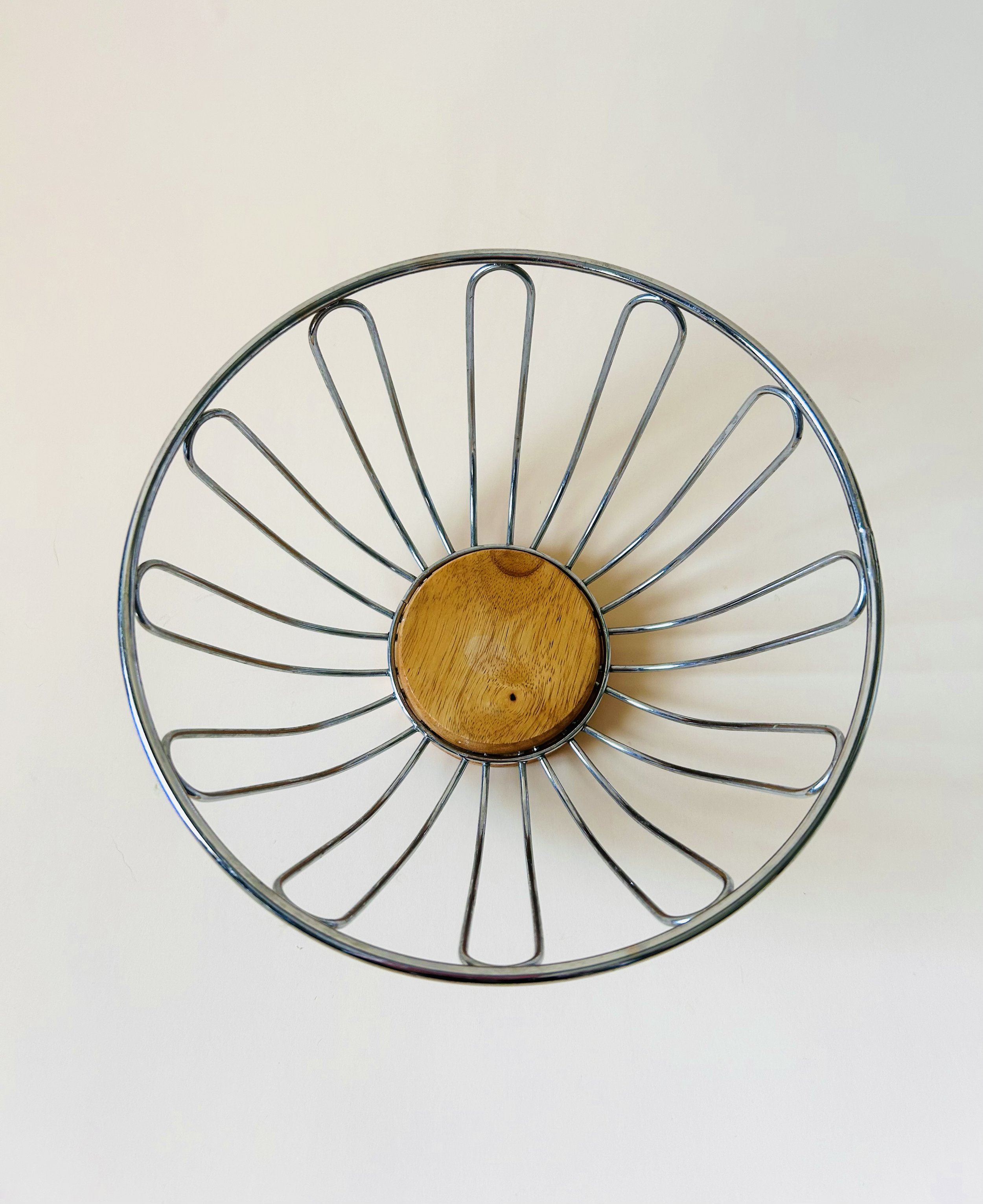 Modern stainless steel wire fruit basket with wooden base, minimalist kitchen storage bowl in natural light