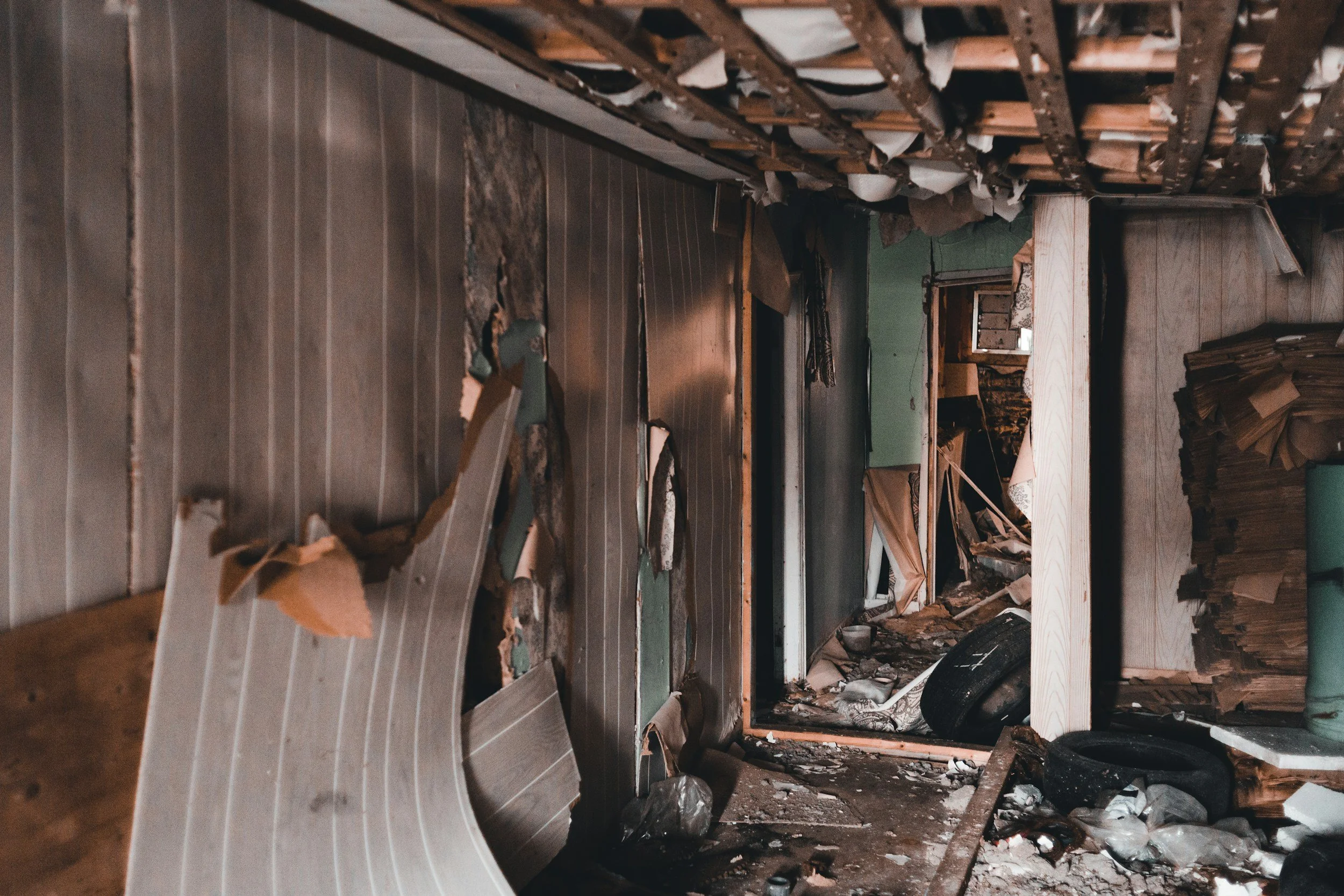 Interior of a severely damaged building with debris, torn walls, and collapsed ceiling in an abandoned or destroyed setting.