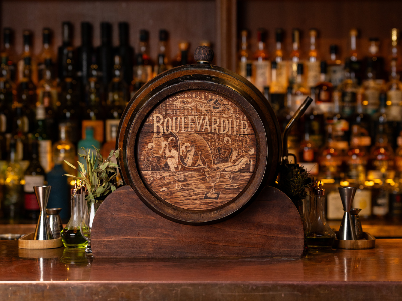 A wooden bar centerpiece with a circular design featuring the word 'Boulevard' and an illustration of a woman at a bar with a cocktail glass, set against a background of liquor bottles.