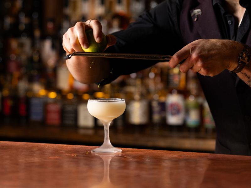 Bartender squeezing lime into a cocktail glass behind the bar.