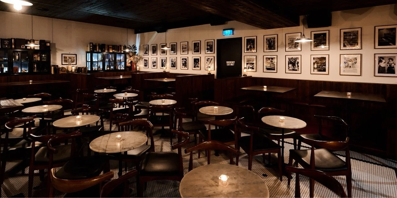 Molly Bar Canberra main bar with round marble tables, wooden chairs, framed photos on the walls, and dim lighting.