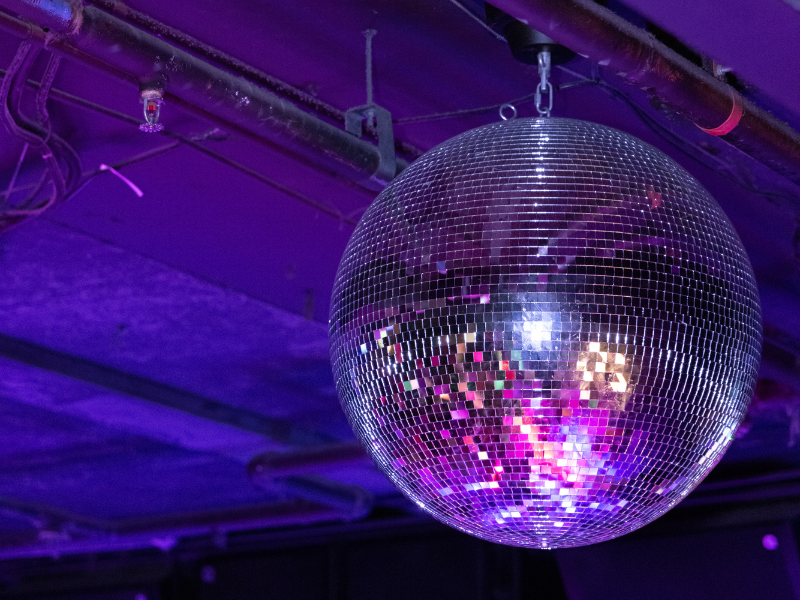A large disco ball hanging from the ceiling with colorful lights reflected on its mirror tiles.