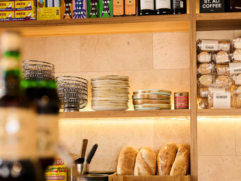 Kitchen or cafe shelf with bowls, plates, loaf of bread, snack packets, and other items.