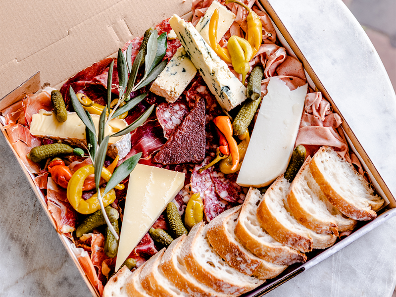 Charcuterie board with sliced bread, assorted cheeses, cured meats, pickles, and olives