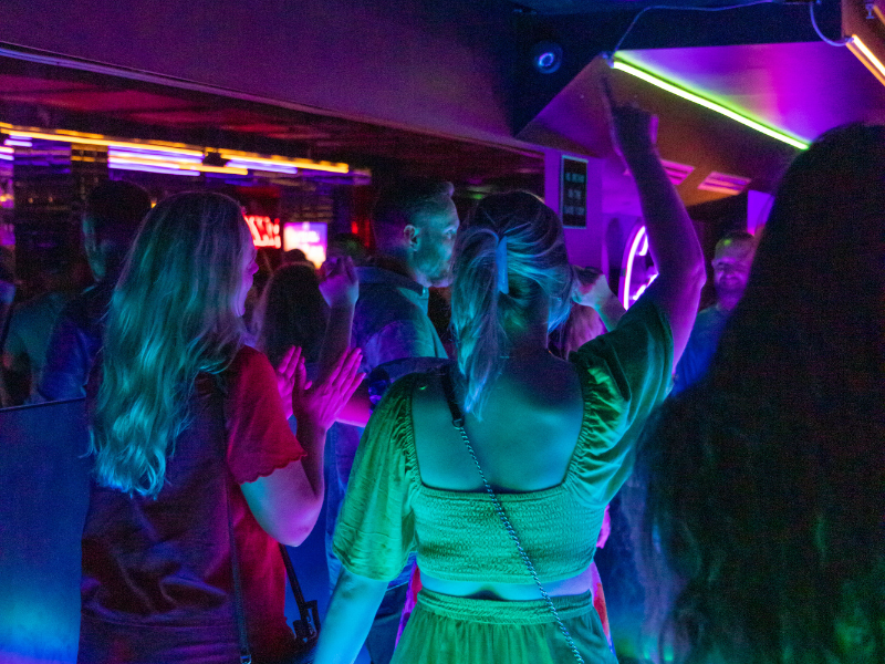 Group of young people dancing in a nightclub with neon and LED lighting.