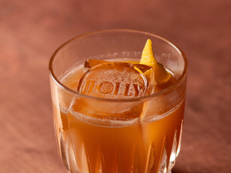 A glass of iced tea with ice cubes, a lemon wedge, and a lemon slice on top.