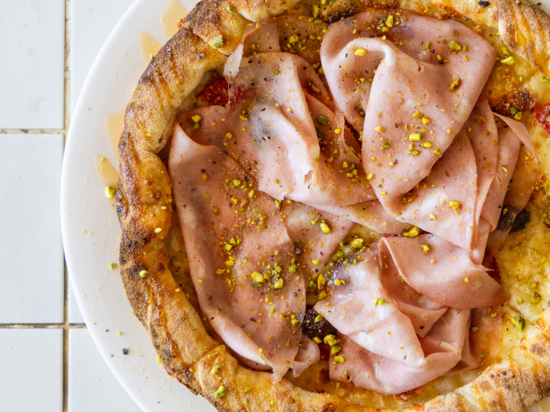 Close-up of a savory pie topped with slices of ham and sprinkled with chopped pistachios.