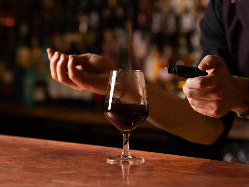 A bartender pouring red wine from a bottle into a glass at a bar.