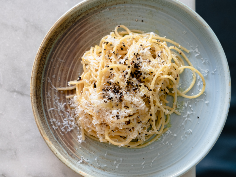 A bowl of spaghetti pasta topped with grated cheese and black pepper.