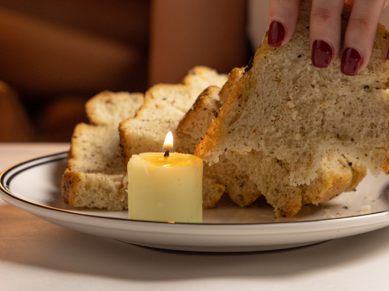 Slices of bread on a plate with a lit candle and a hand holding a large piece of bread