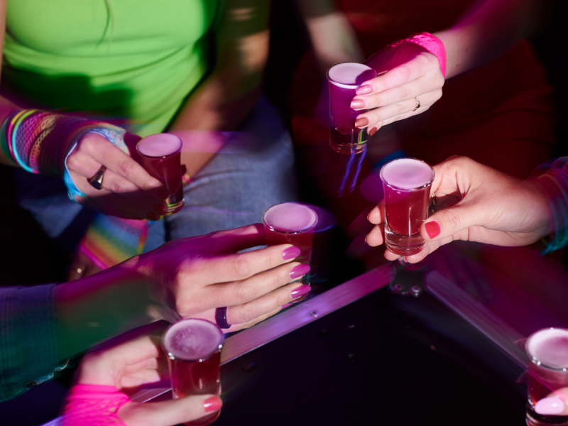 People holding shot glasses filled with red liquid in a social setting.
