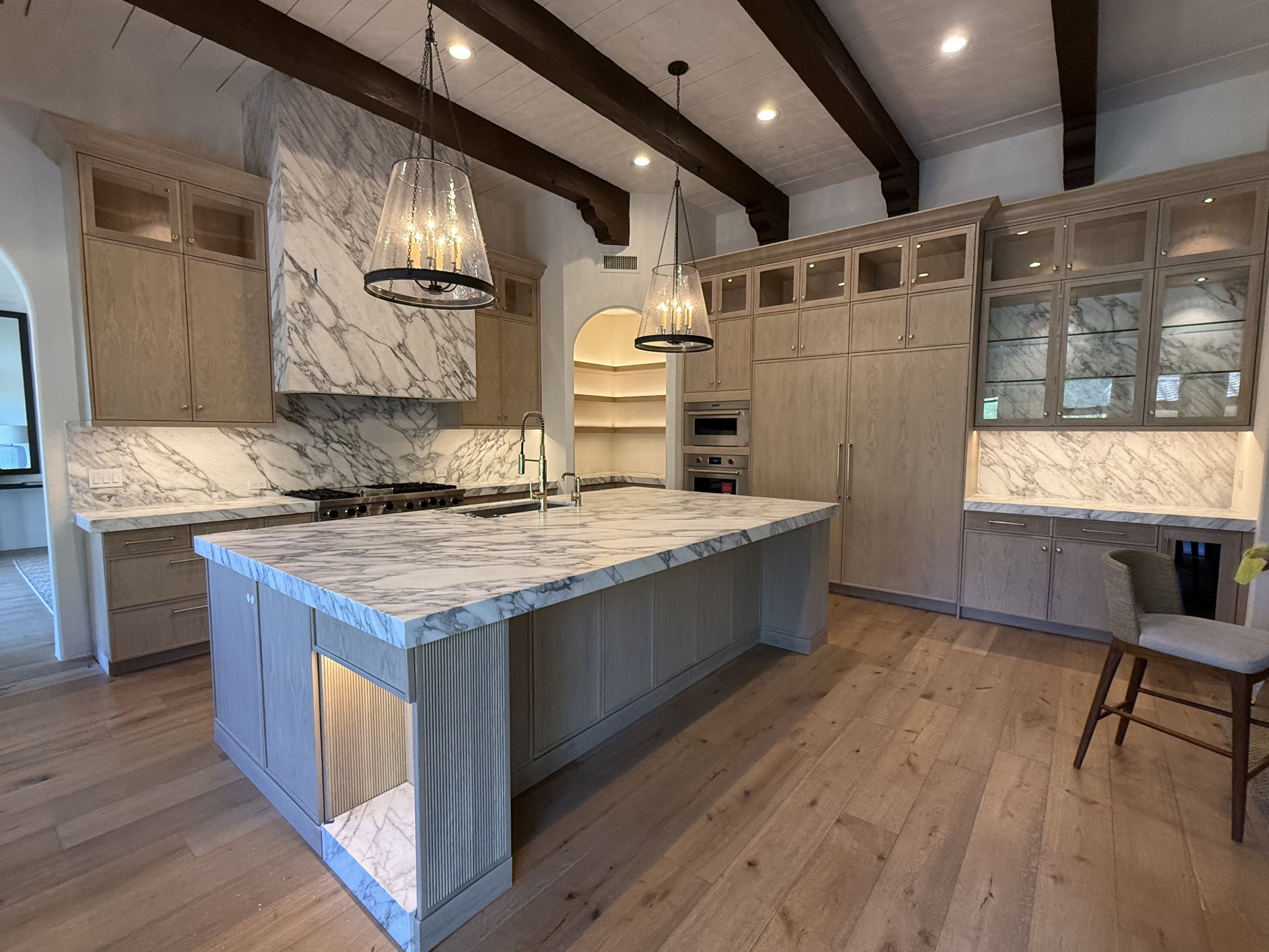 Modern kitchen with marble island, wooden cabinetry, and high ceilings with exposed wooden beams.