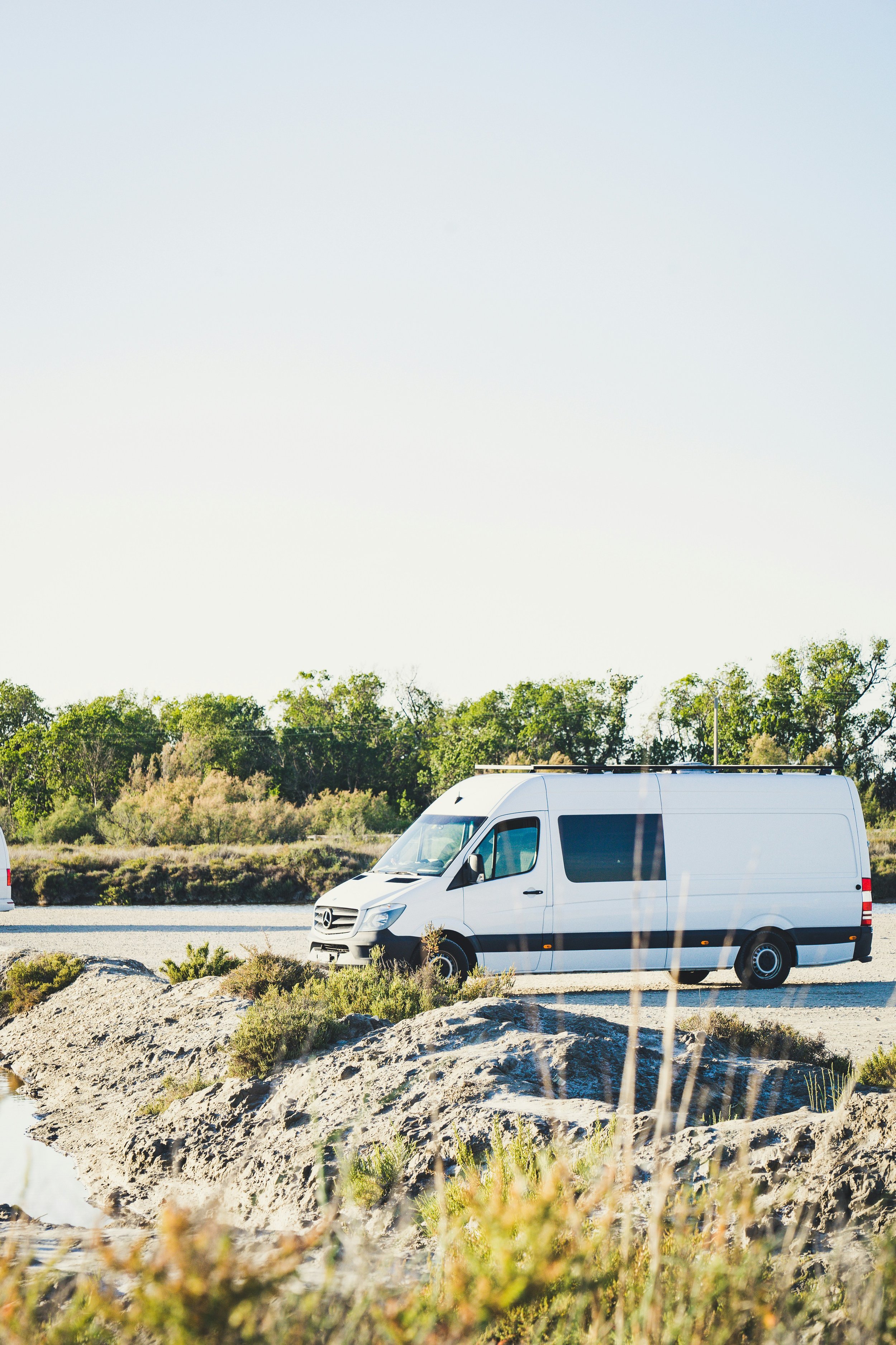 A white van parked on a roadside with greenery in the background and rocks in the foreground.