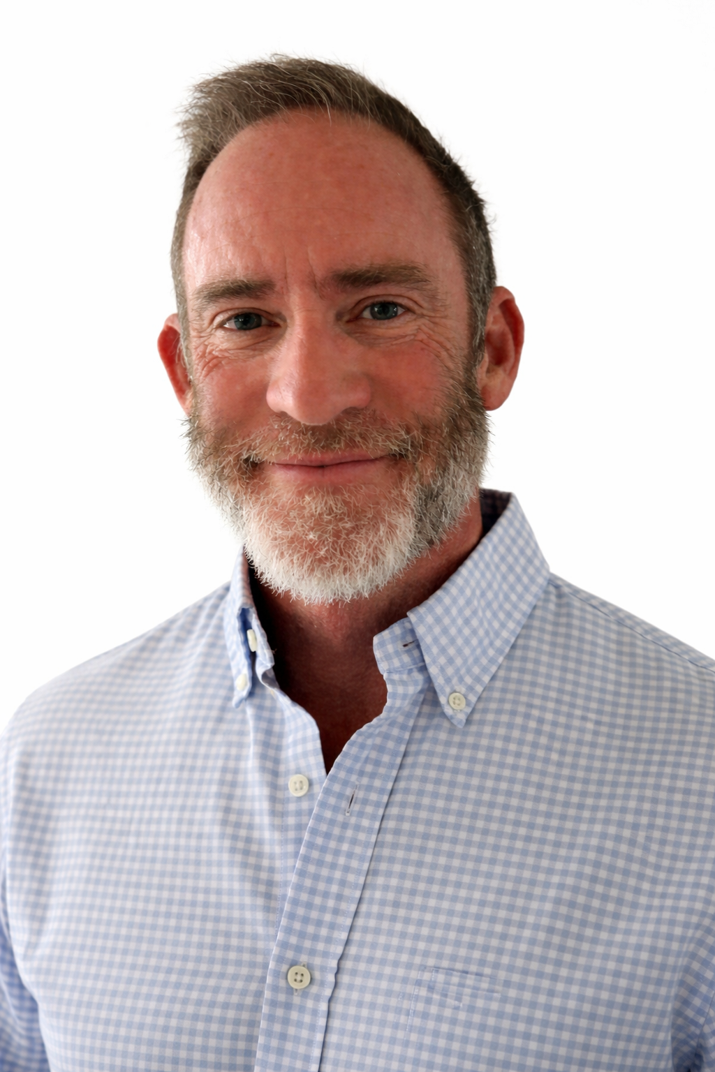 A middle-aged man with a salt-and-pepper beard and hair, smiling, wearing a light blue checkered button-up shirt. Director of Construction, Chad Norman.
