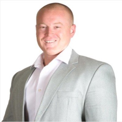 A smiling man in a light gray blazer and white shirt posing against a plain white background. COO, Ben Mies.
