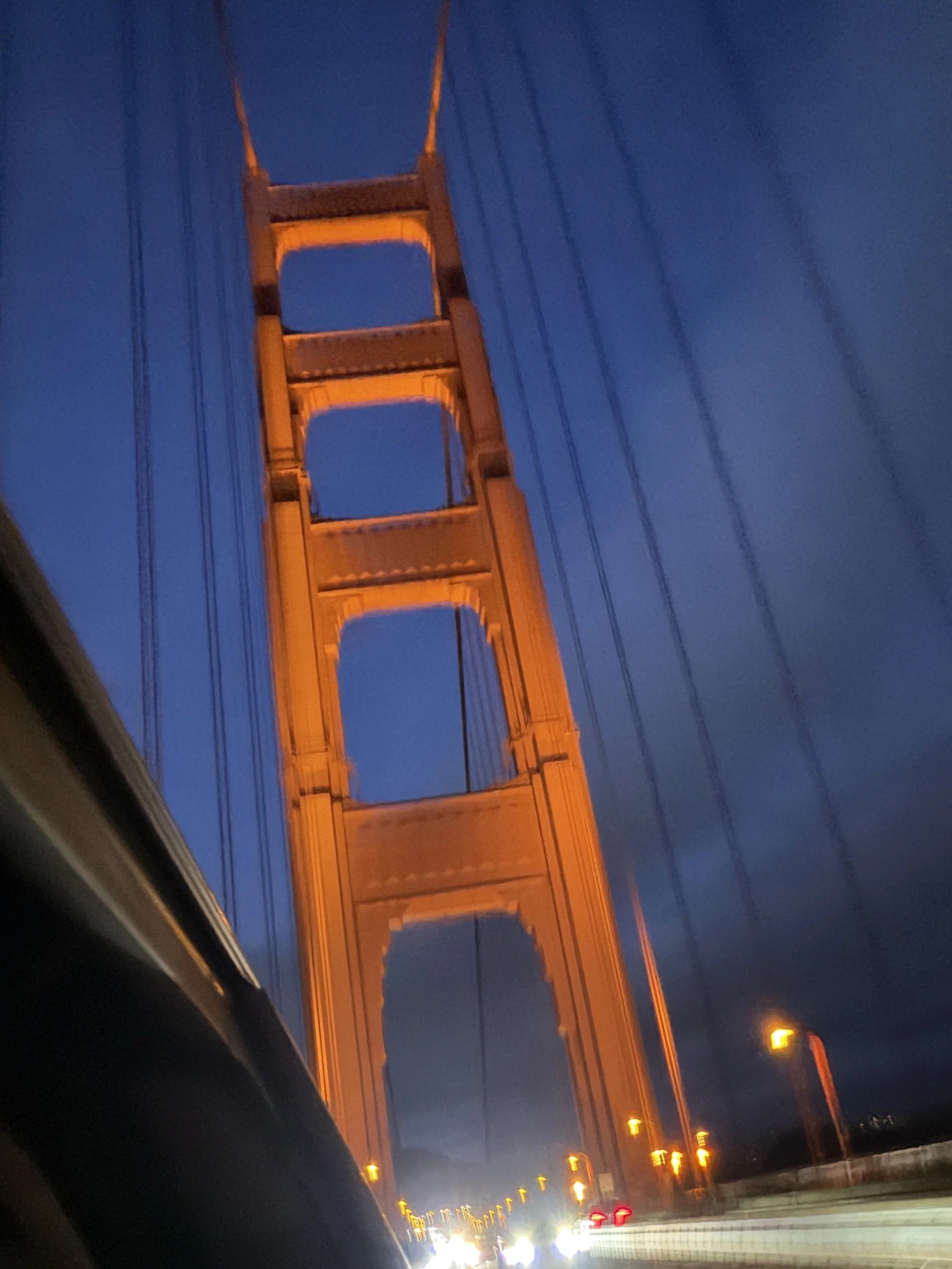 The Golden Gate Bridge illuminated in orange at dusk or early evening with cars on the bridge.
