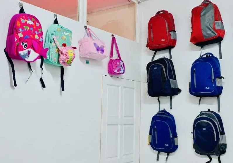 Colorful backpacks and lunch bags displayed on a white wall in a store or classroom setting.