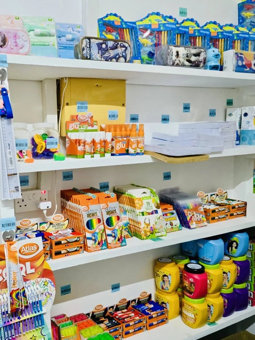 School supplies on store shelves including glue sticks, notebooks, colored pens, and containers of crayons.