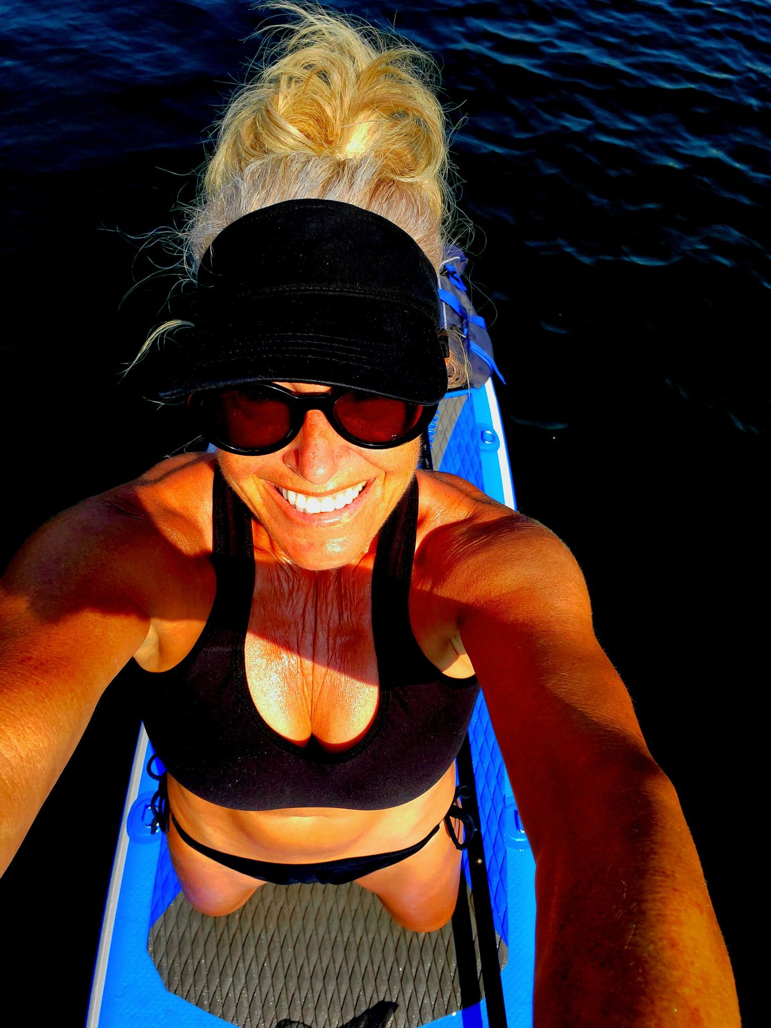Person in black bathing suit taking a selfie while paddleboarding on water in Oxnard, Ca on a paddle board rental by winged not wired watersports