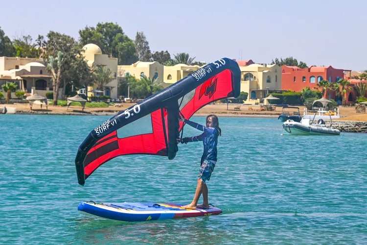 Group of kids in helmets on water with paddle boards and wings, engaging in watersport activity, by winged not wired watersports