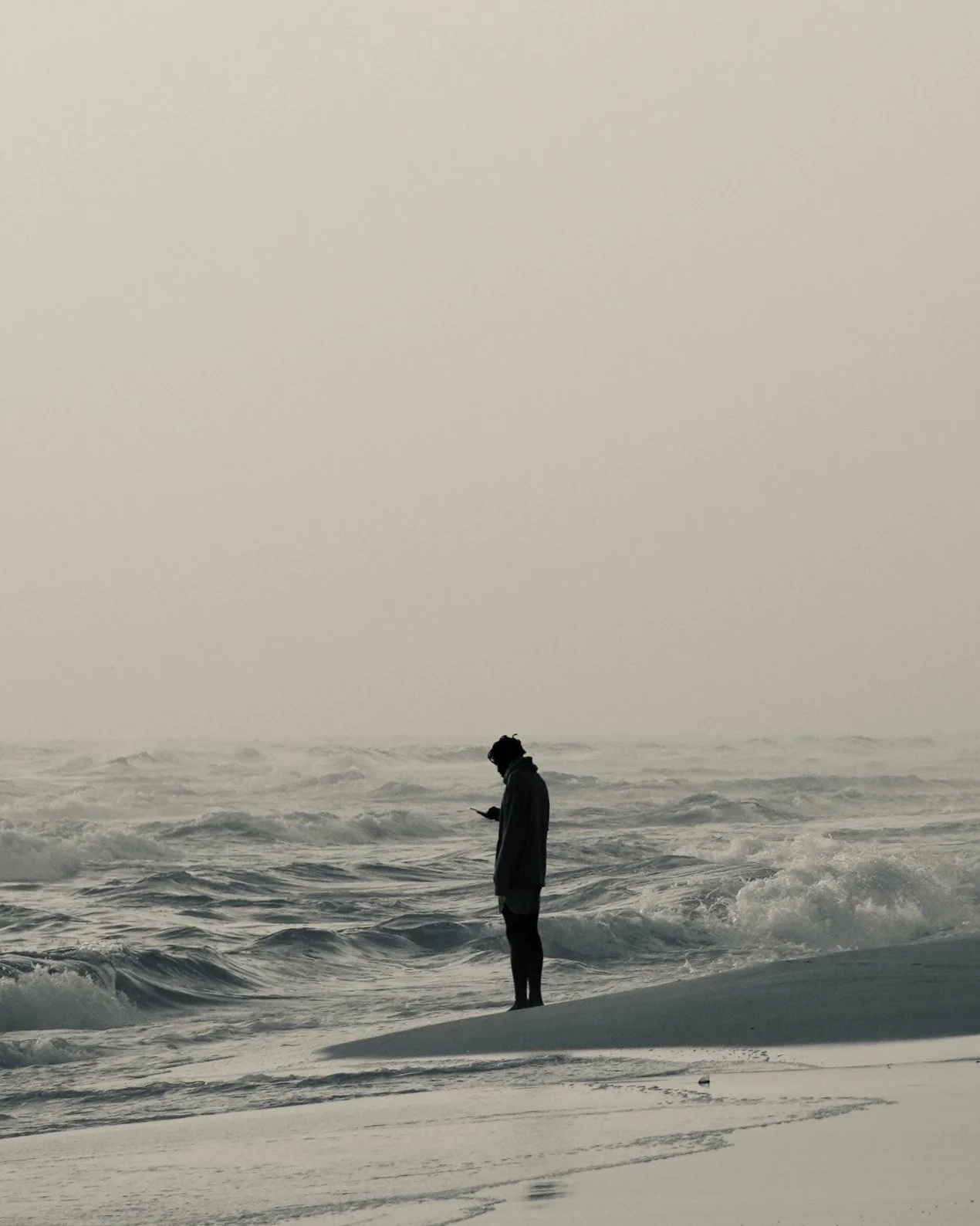 Lonely figure looking at phone at the beach.