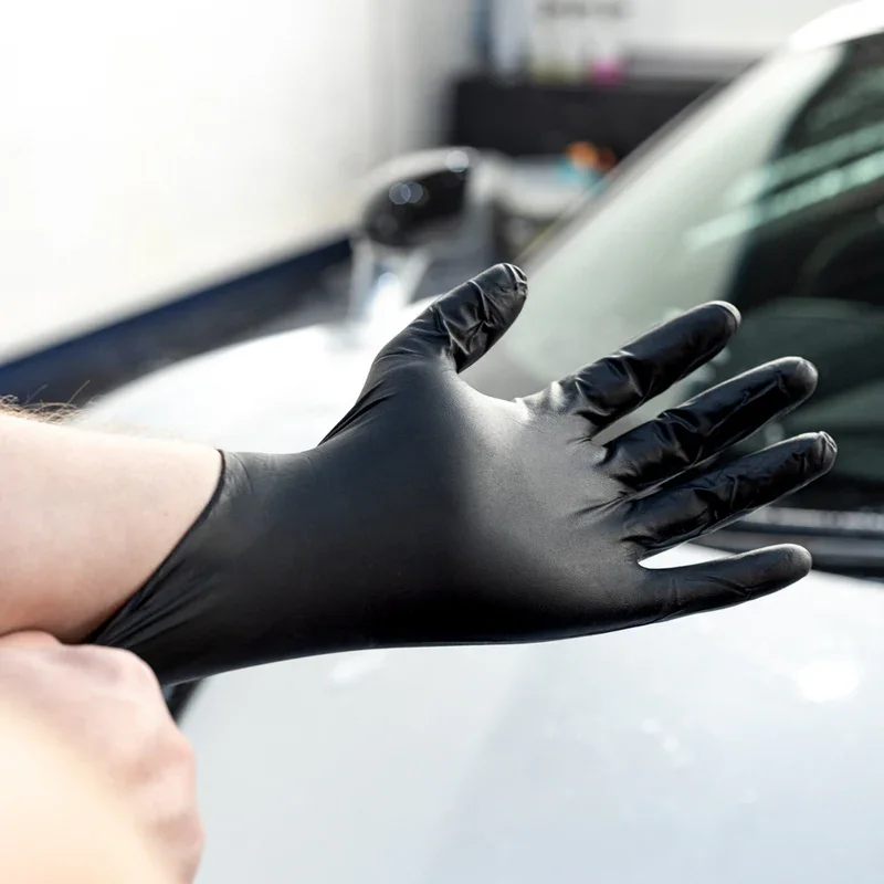 A person wearing a black glove touching a white car in a garage or auto service area or a mobile detailer glove