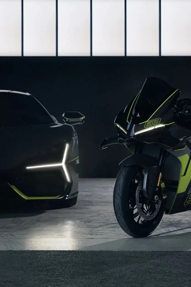 A black Lamborghini sports car and a black and green Ducati motorcycle in a modern indoor setting with large windows.