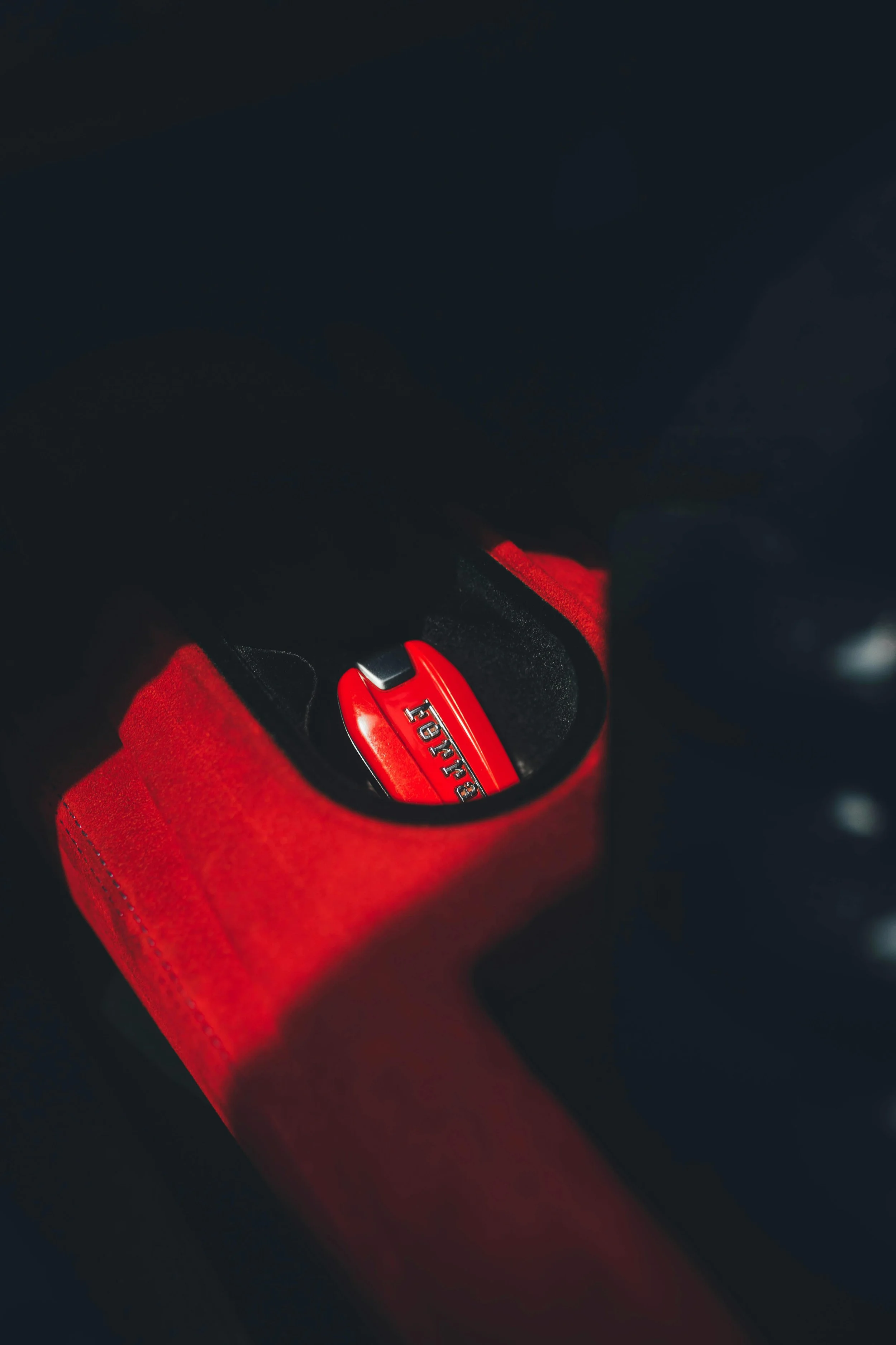 Close-up of a red Ferrari key fob inside a red pocket or holder, with a dark background inside the car.