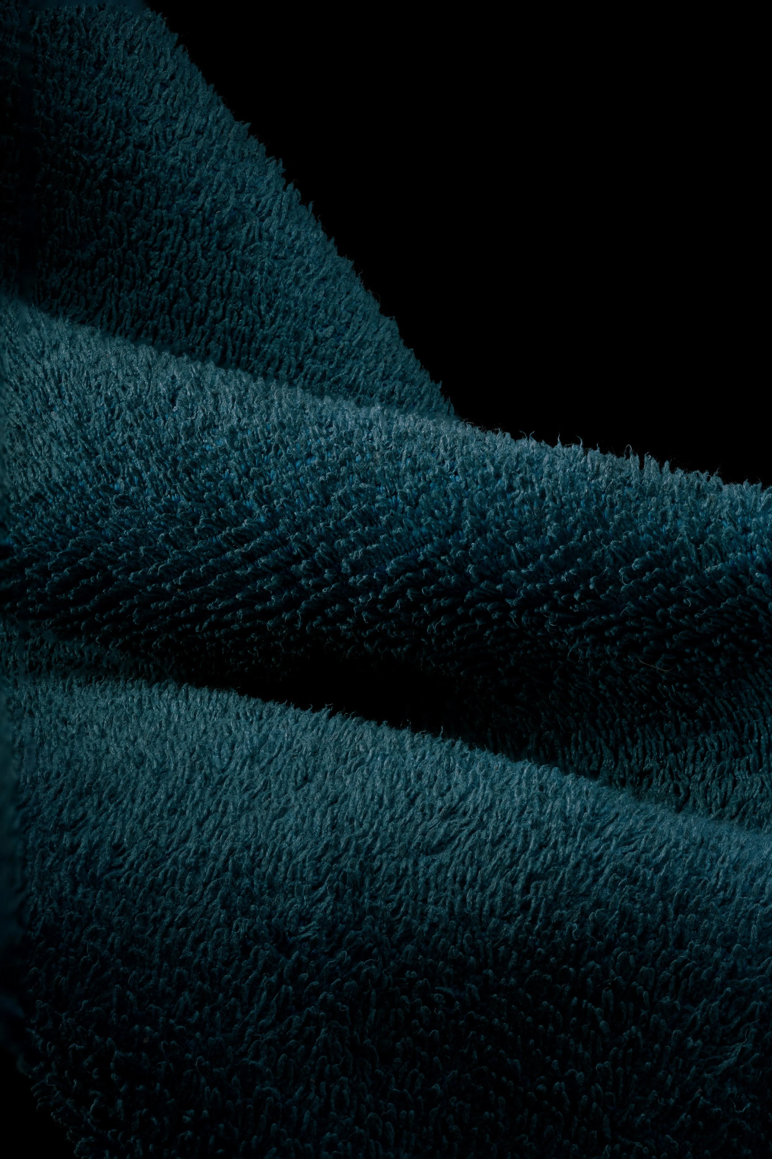 Close-up of dark teal fabric with a textured, fuzzy surface, draped against a black background.