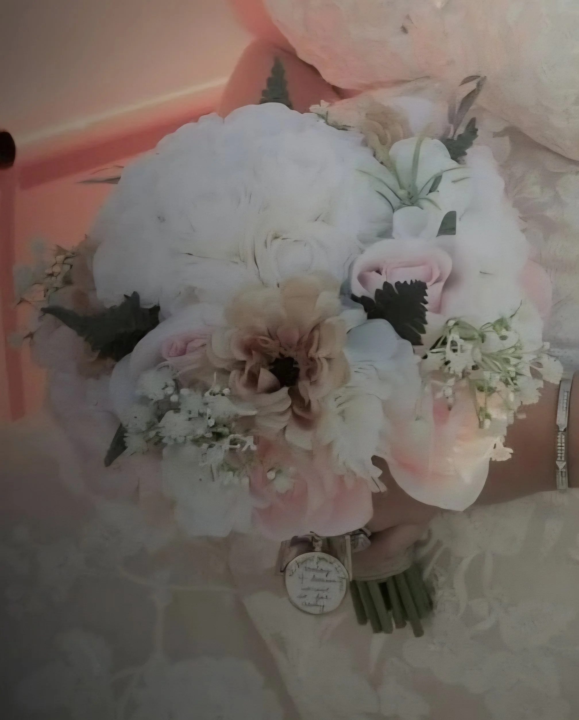 A floral arrangement with white, pink, and beige flowers, including lilies, roses, and orchids, placed on a reflective surface.