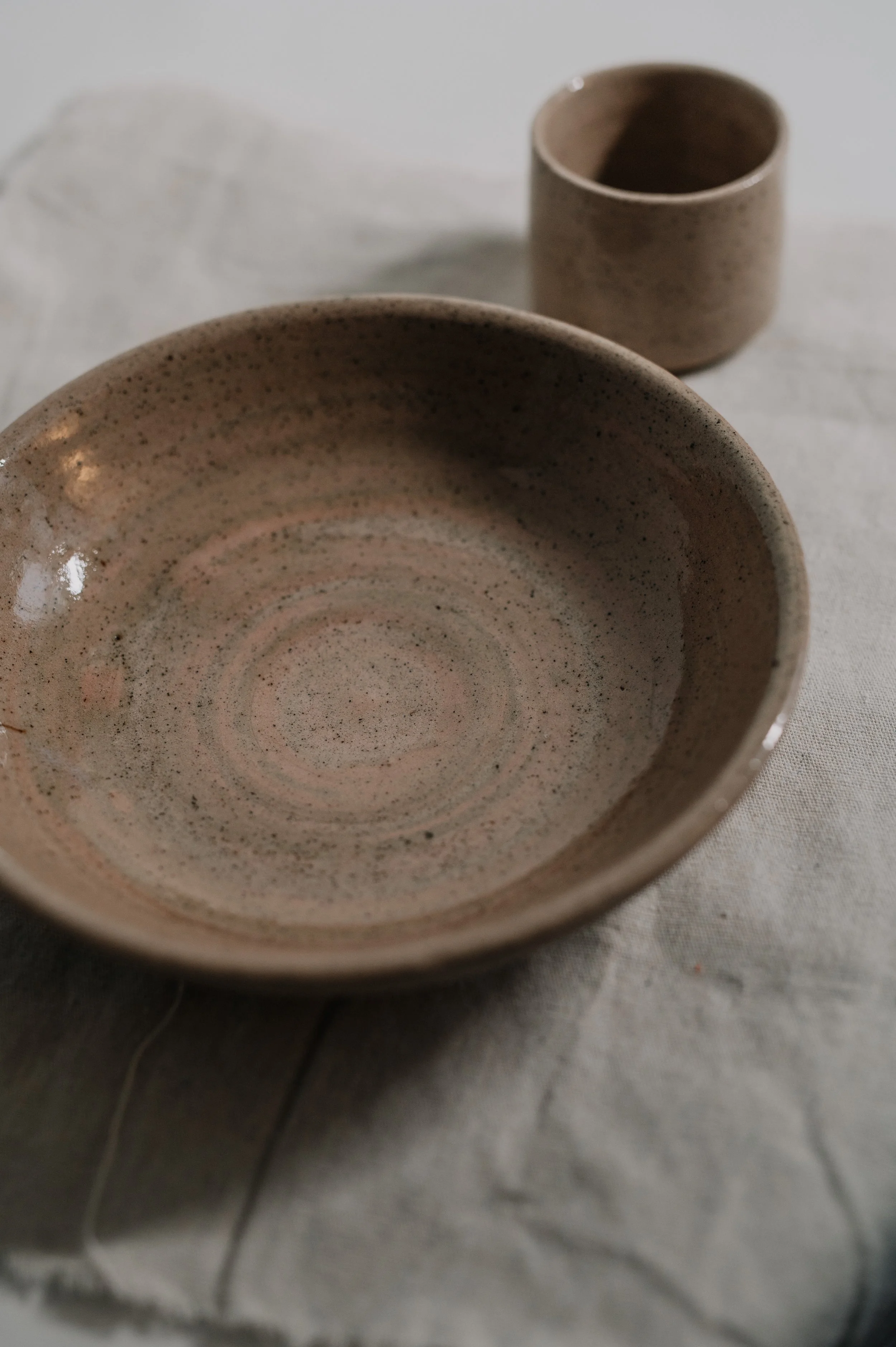 A speckled ceramic bowl and a matching ceramic cup are placed on a white cloth surface.