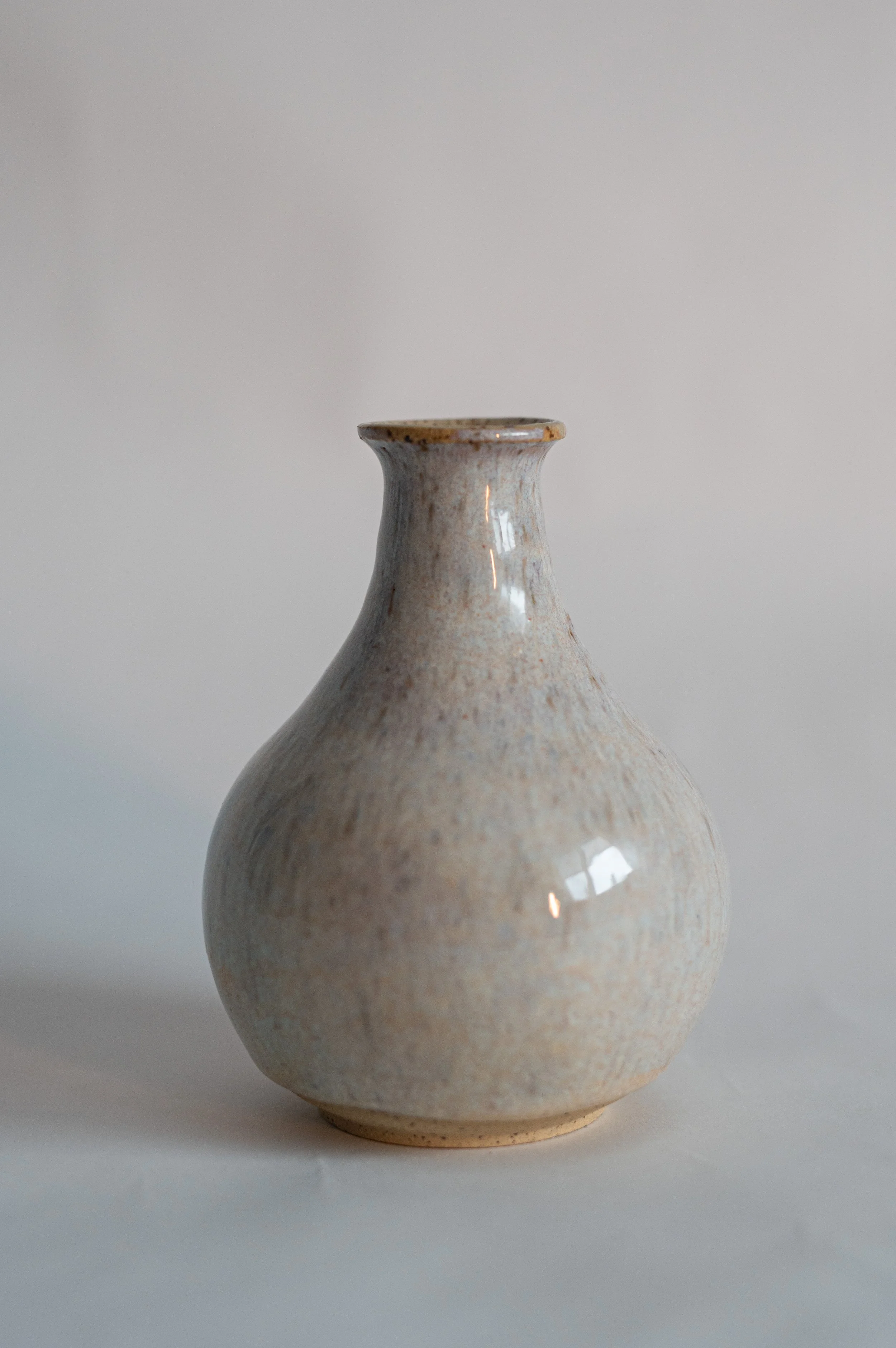 A beige ceramic vase with a narrow neck and round body, placed against a plain white background.
