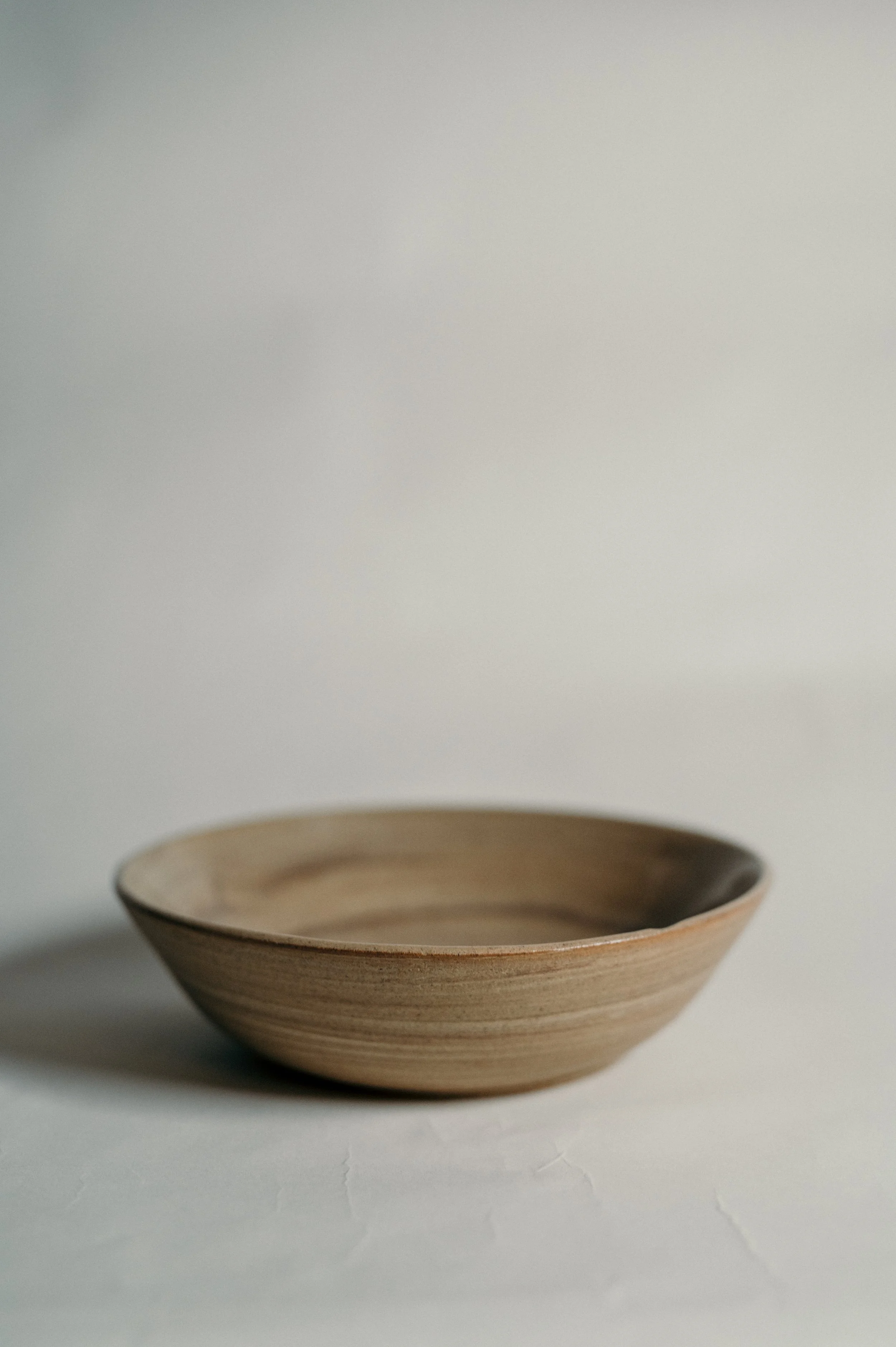 A shallow, beige ceramic bowl with a smooth, matte finish placed on a plain white surface against a white background.
