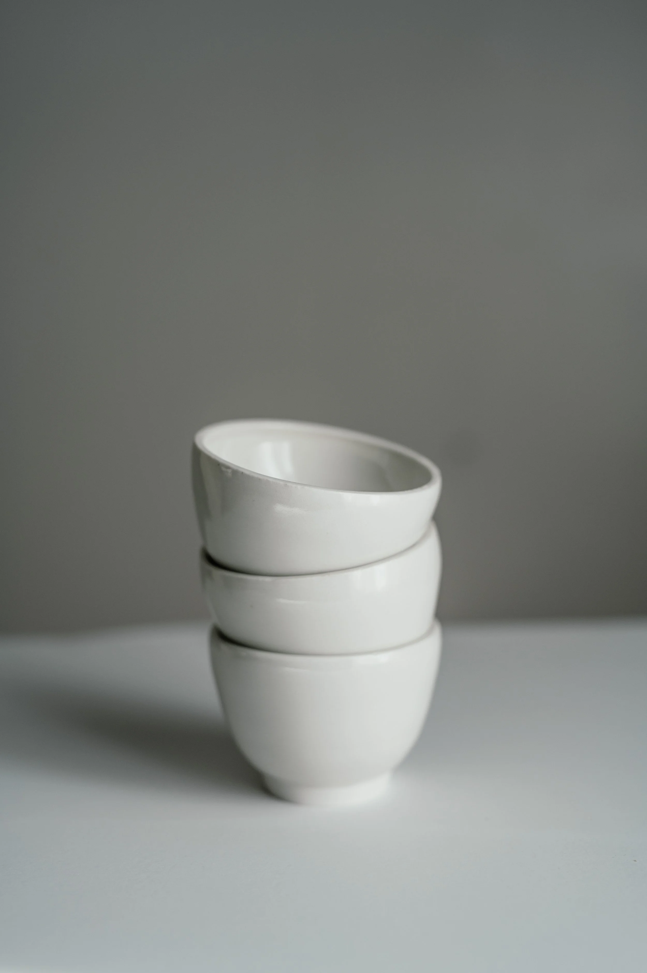 Three stacked white ceramic bowls on a light surface with a plain gray background.