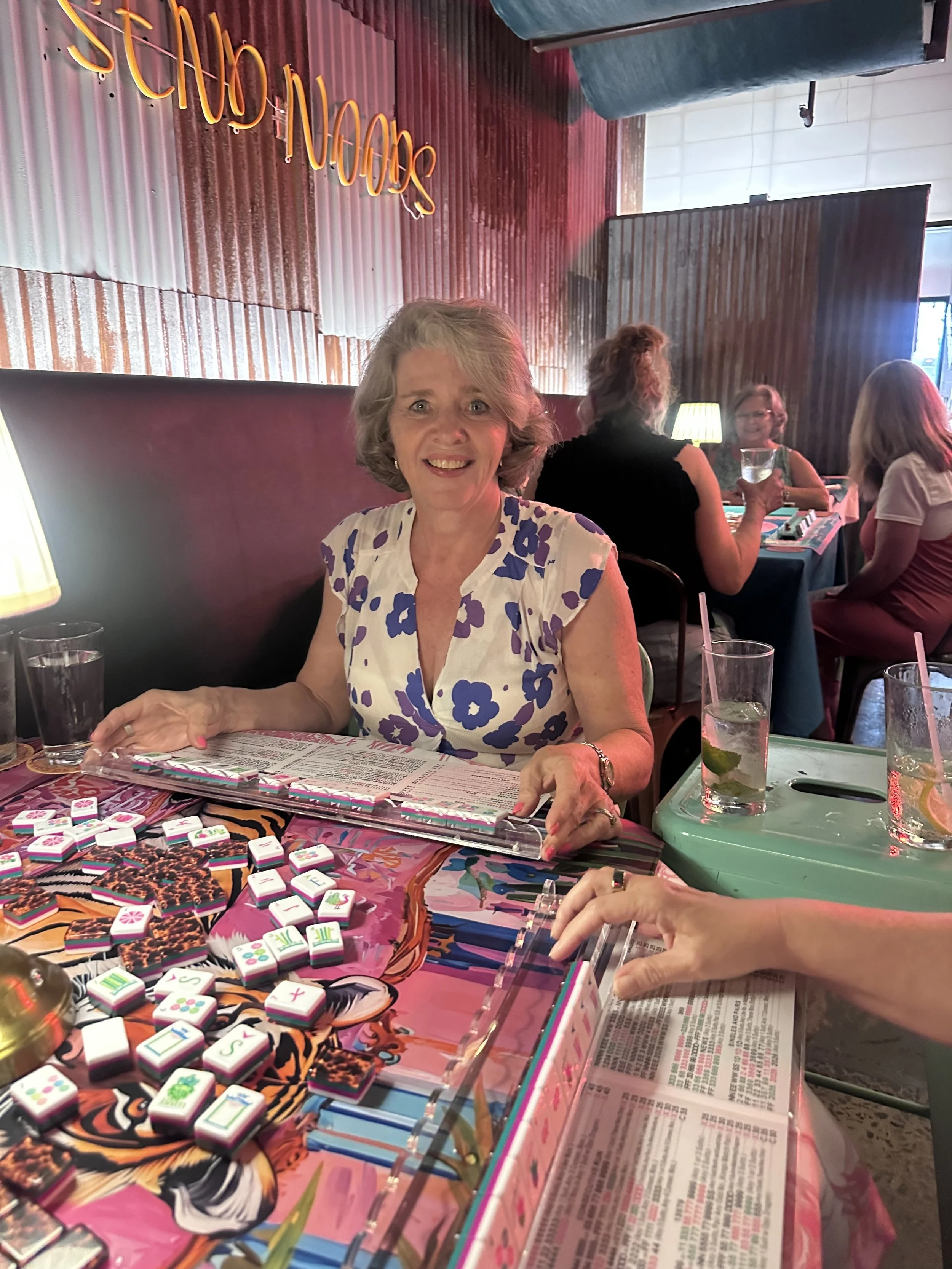 Women playing a game with colorful tiles and slot pieces at a table in a restaurant.