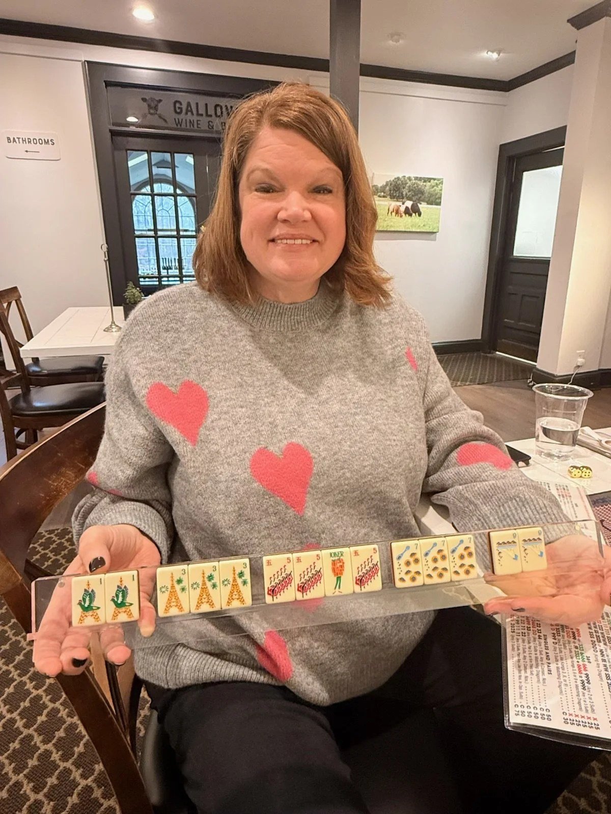 A woman with red hair sitting at a table displaying a set of Mahjong tiles.