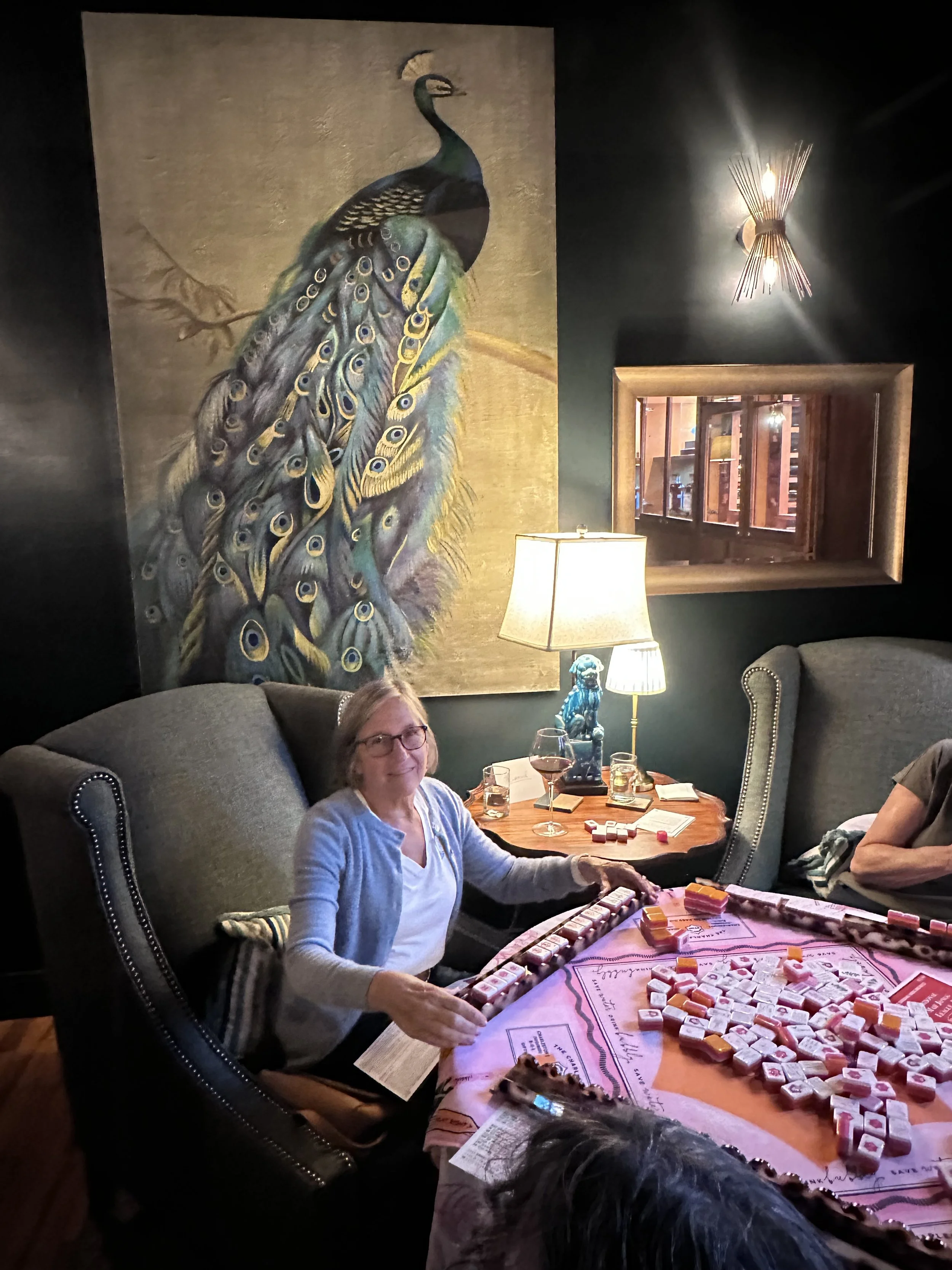 Woman playing American Mahjong in a cozy lounge with a peacock painting