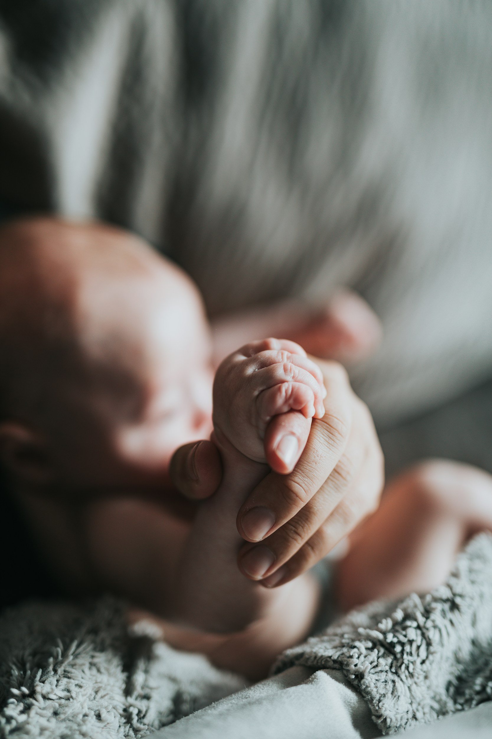 Close-up of a newborn baby holding an adult's finger, lying on a textured blanket.