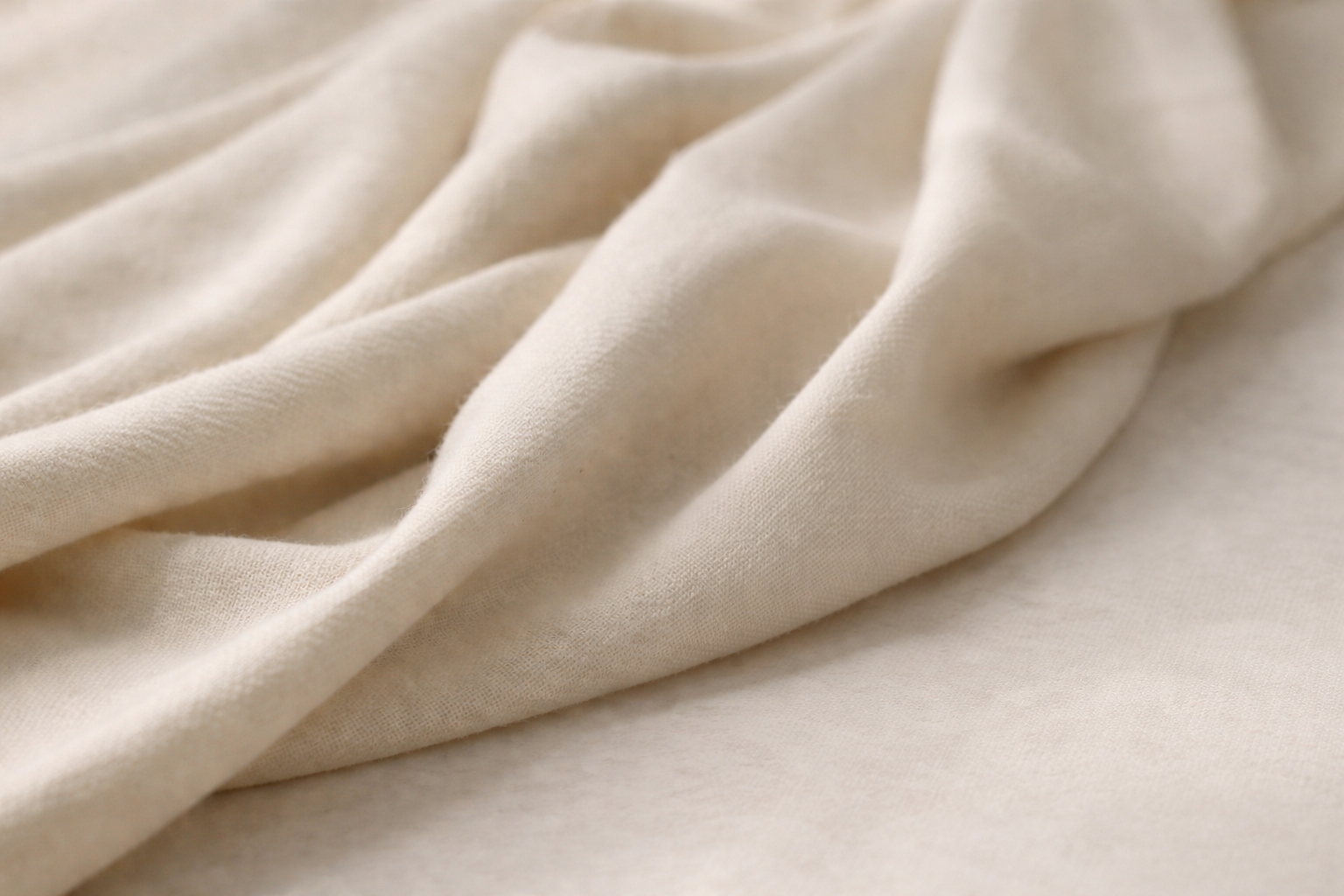Close-up of beige or off-white fabric with soft folds and gentle texture.