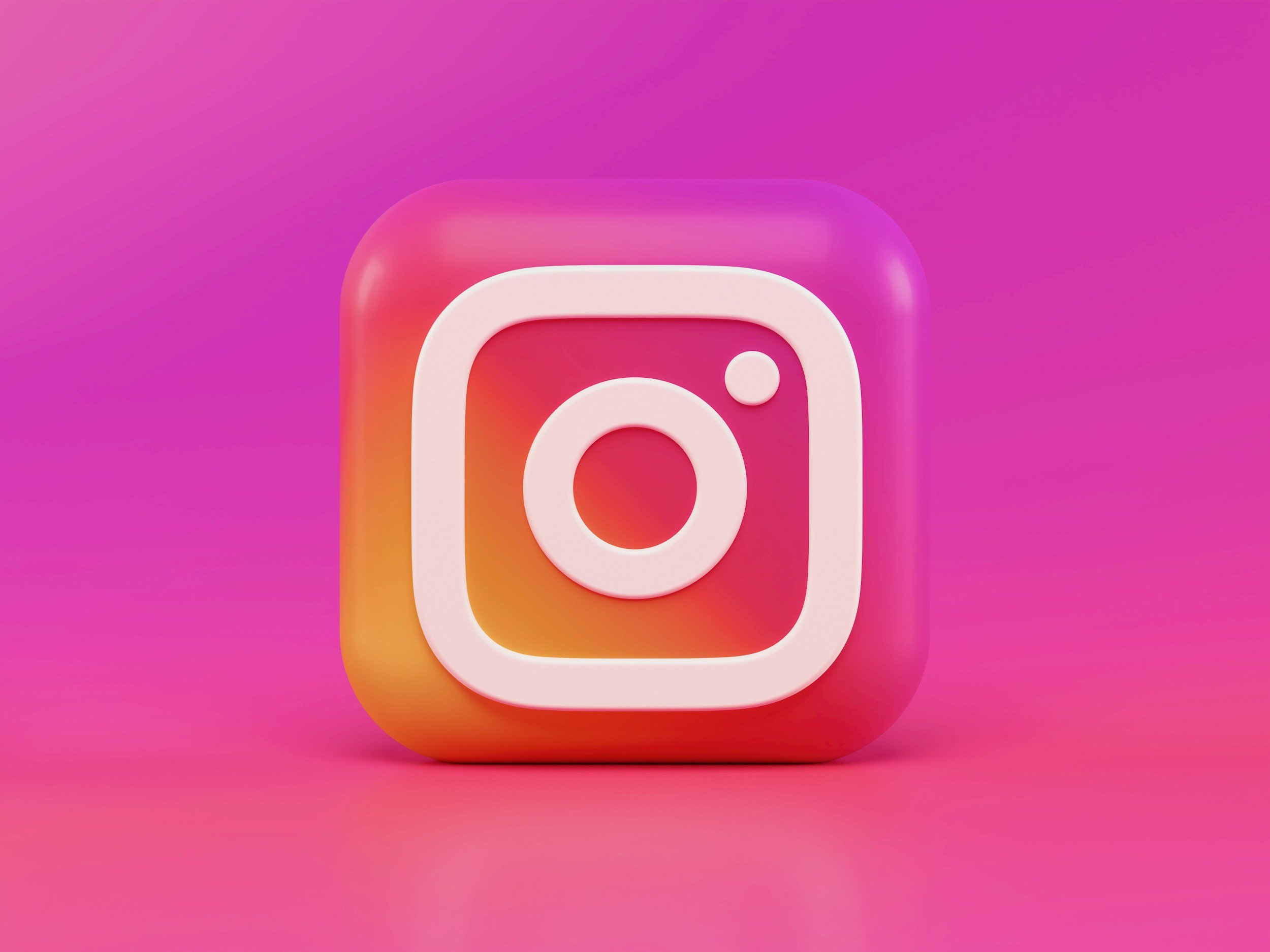 Close-up of a 3D Instagram logo icon on a pink and orange background.
