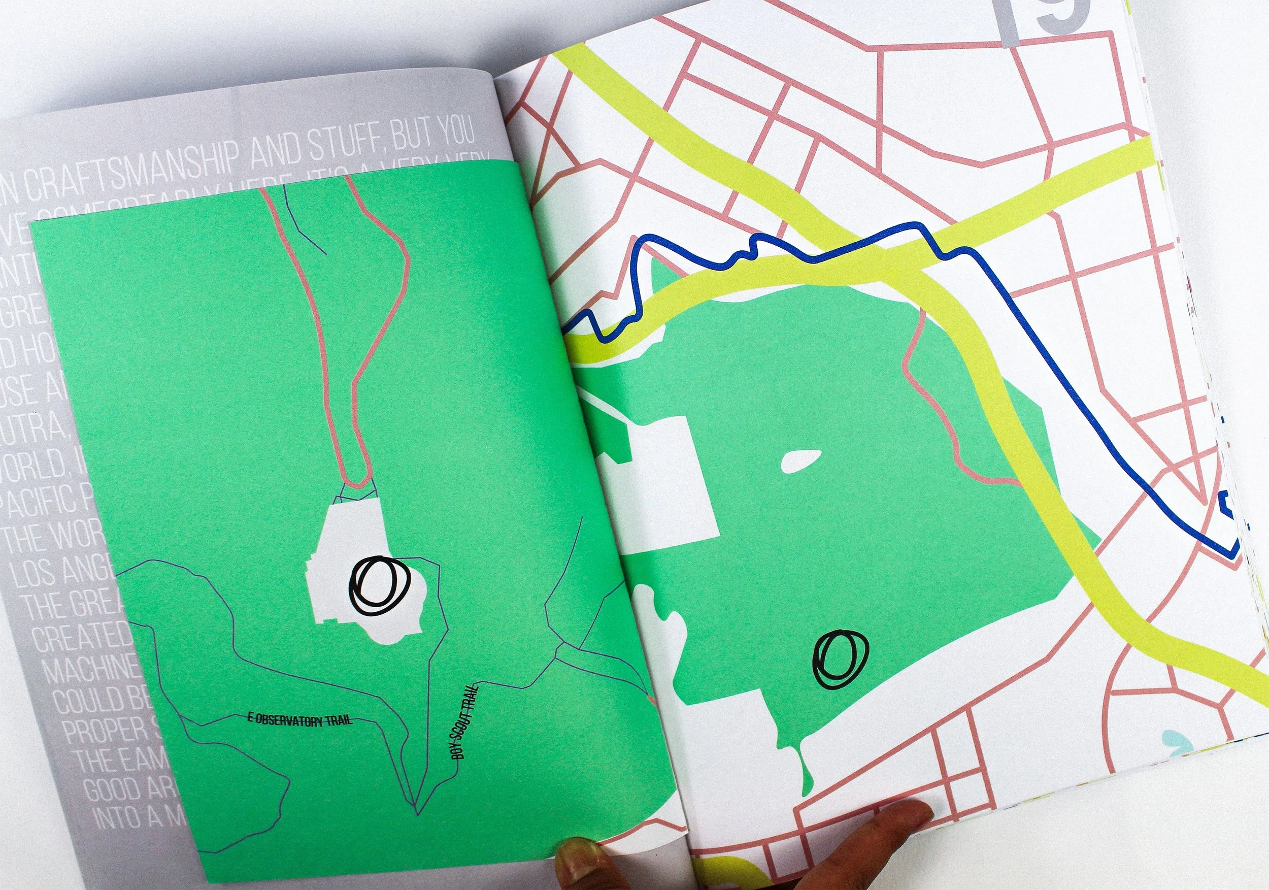 Open magazine or book showing maps and trails of a park or outdoor area, with some green-colored sections and labeled paths