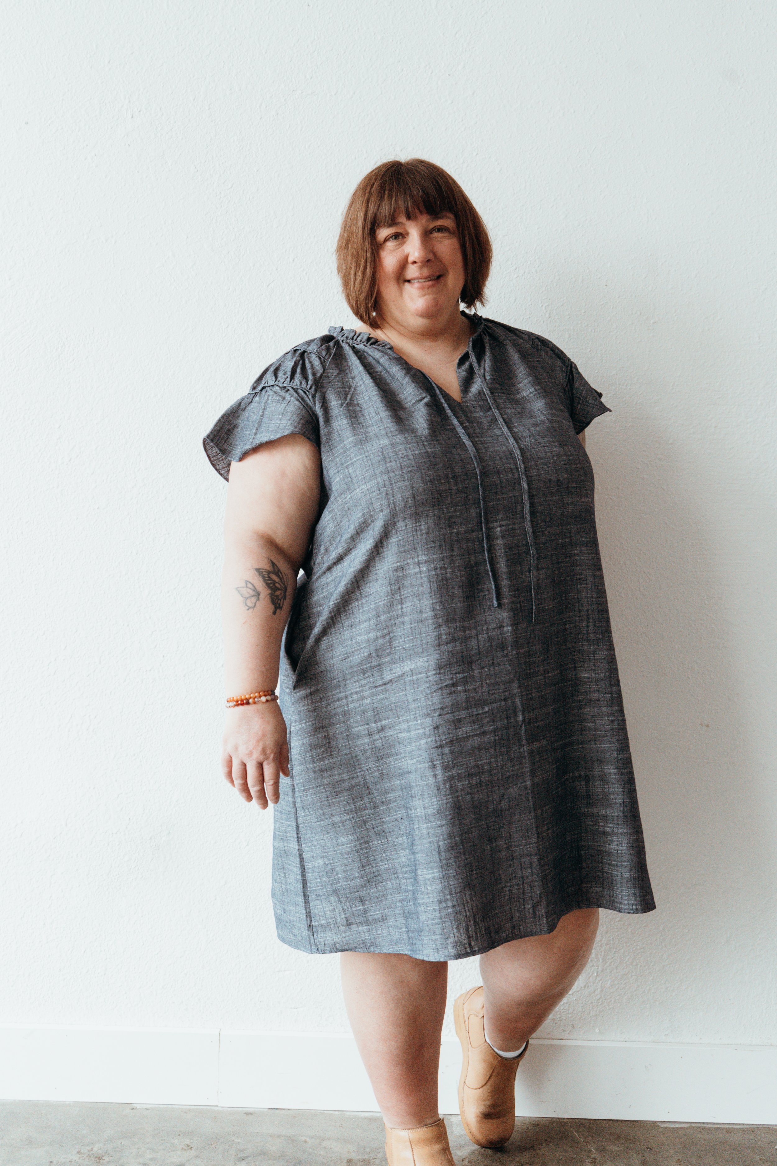 Marci's headshot standing against a white wall smiling with one arm down.