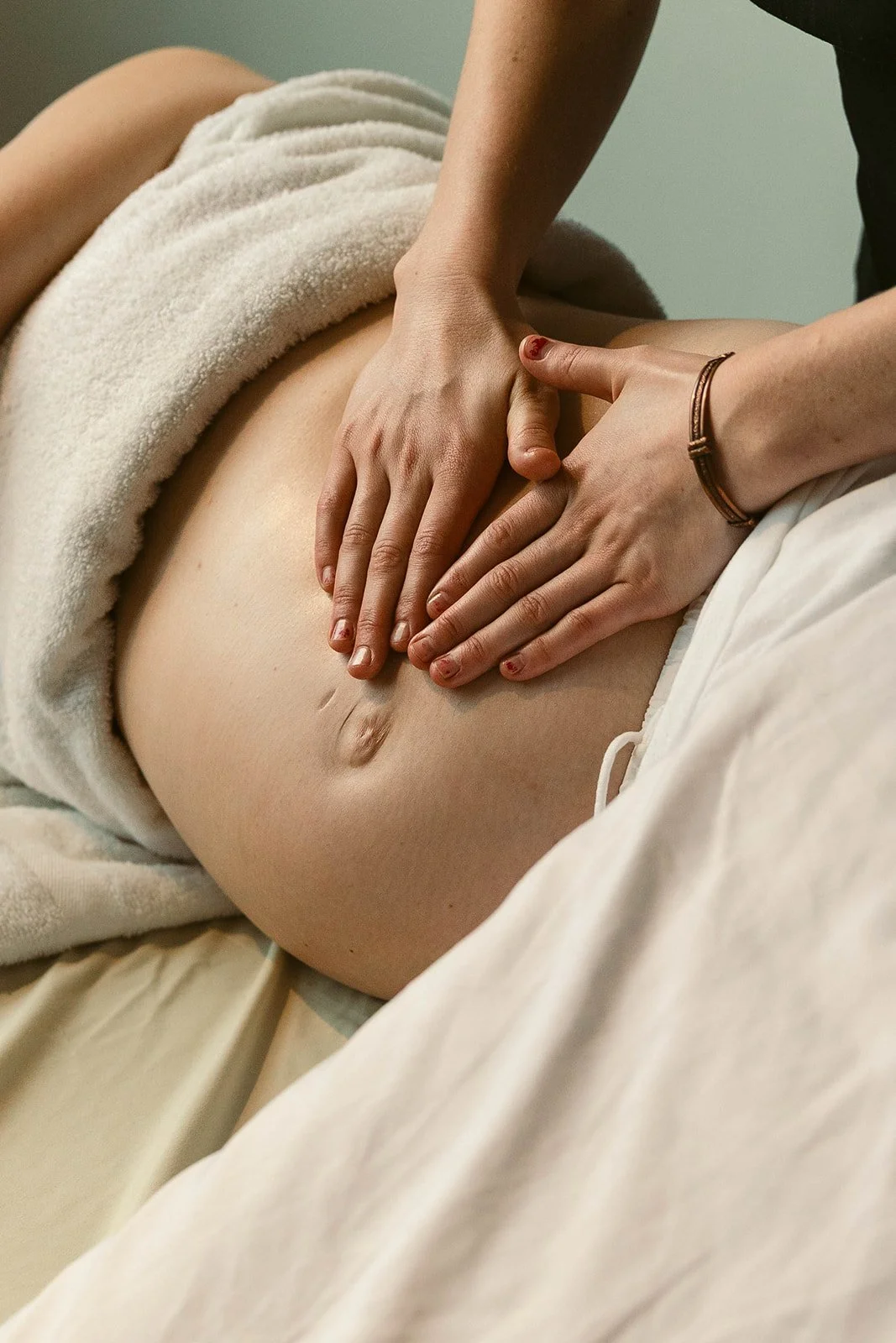A person receiving a massage on their pregnant stomach, with a towel draped over their waist.